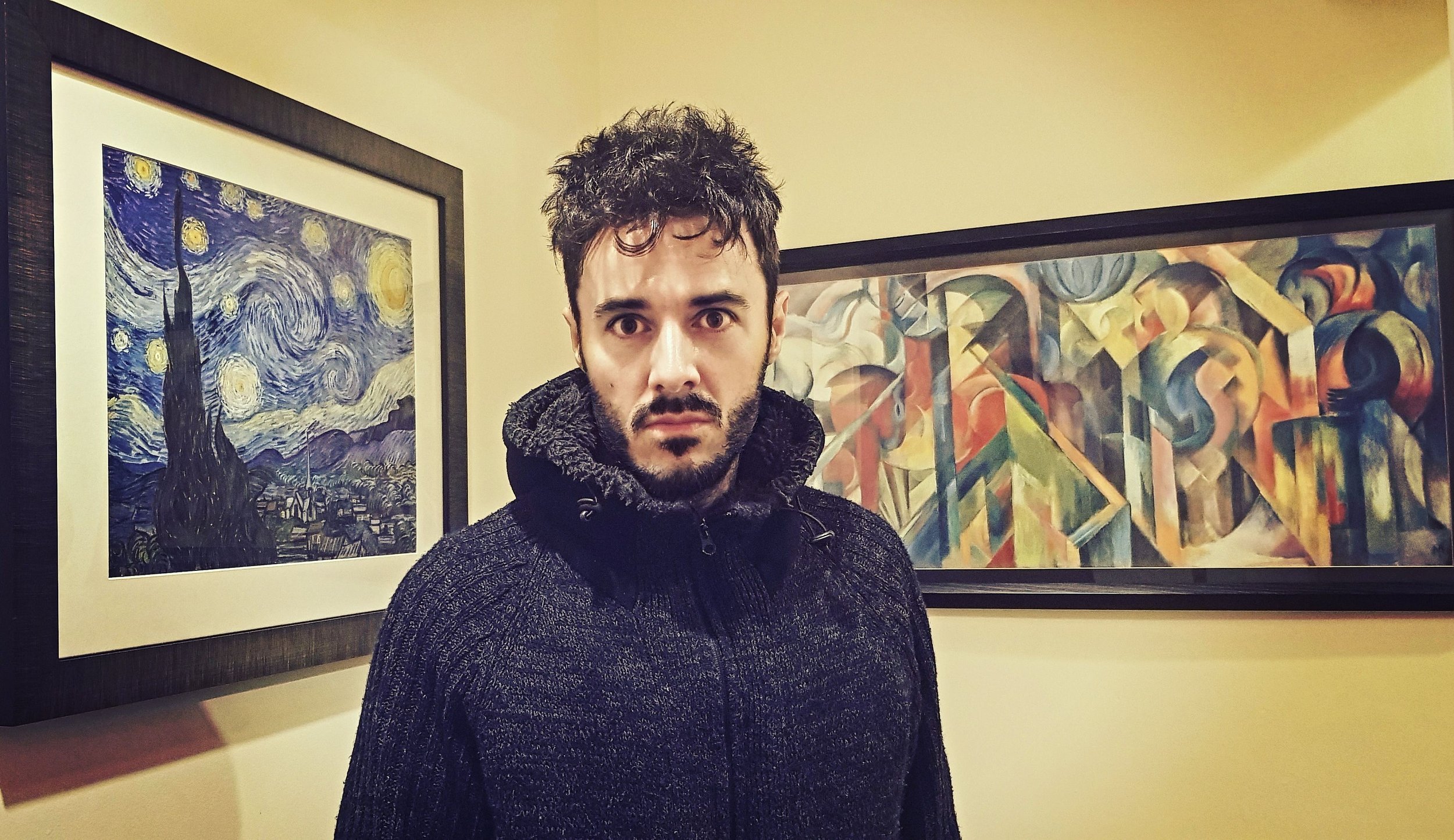 James Kennedy, the singer songwriter from Wales posing in his home in front of paintings 