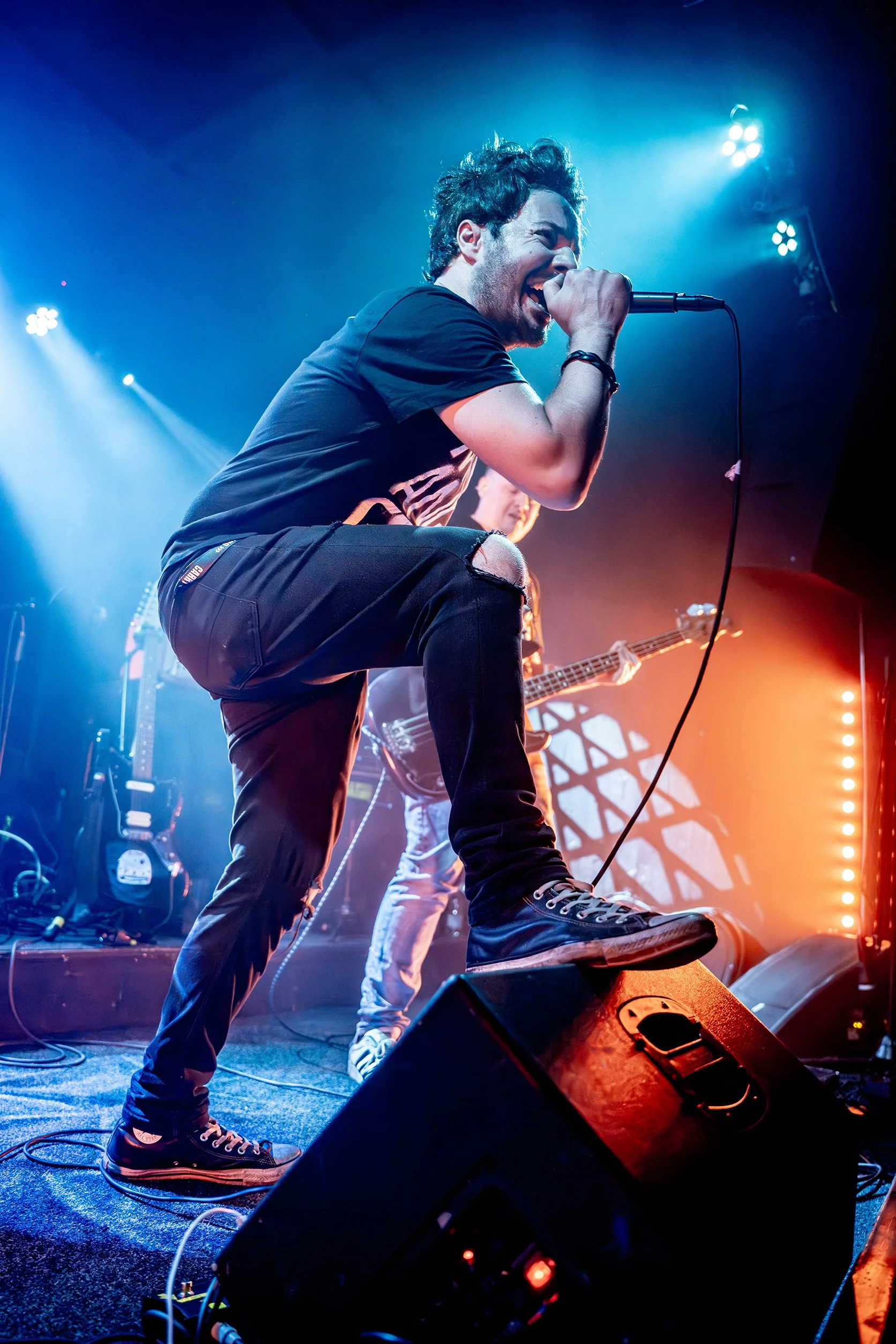 James Kennedy, the singer, author and podcaster singing live on stage with his band 'James Kennedy and The Underdogs' standing on the stage monitor during a concert 