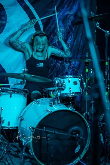 Aggy Nowicka, the drummer for the Welsh band 'James Kennedy and The Underdogs' about to hit her drums during a concert with the band under blue stage lights 