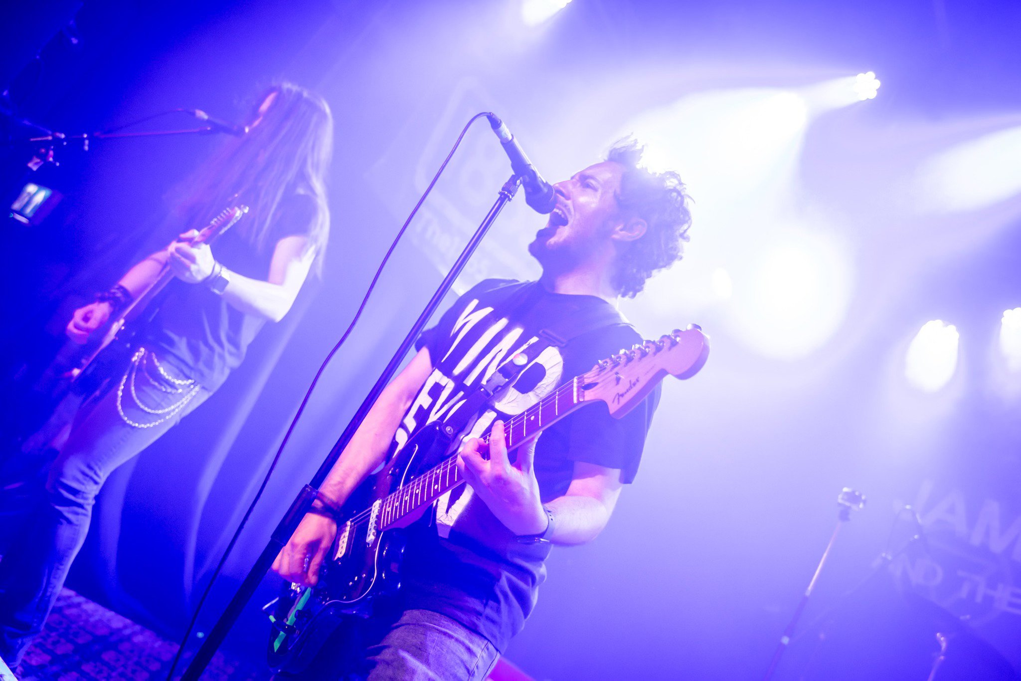 James Kennedy, the singer and author on stage with the Welsh rock band 'James Kennedy and The Underdogs' playing guitar and singing under purple stage lights 
