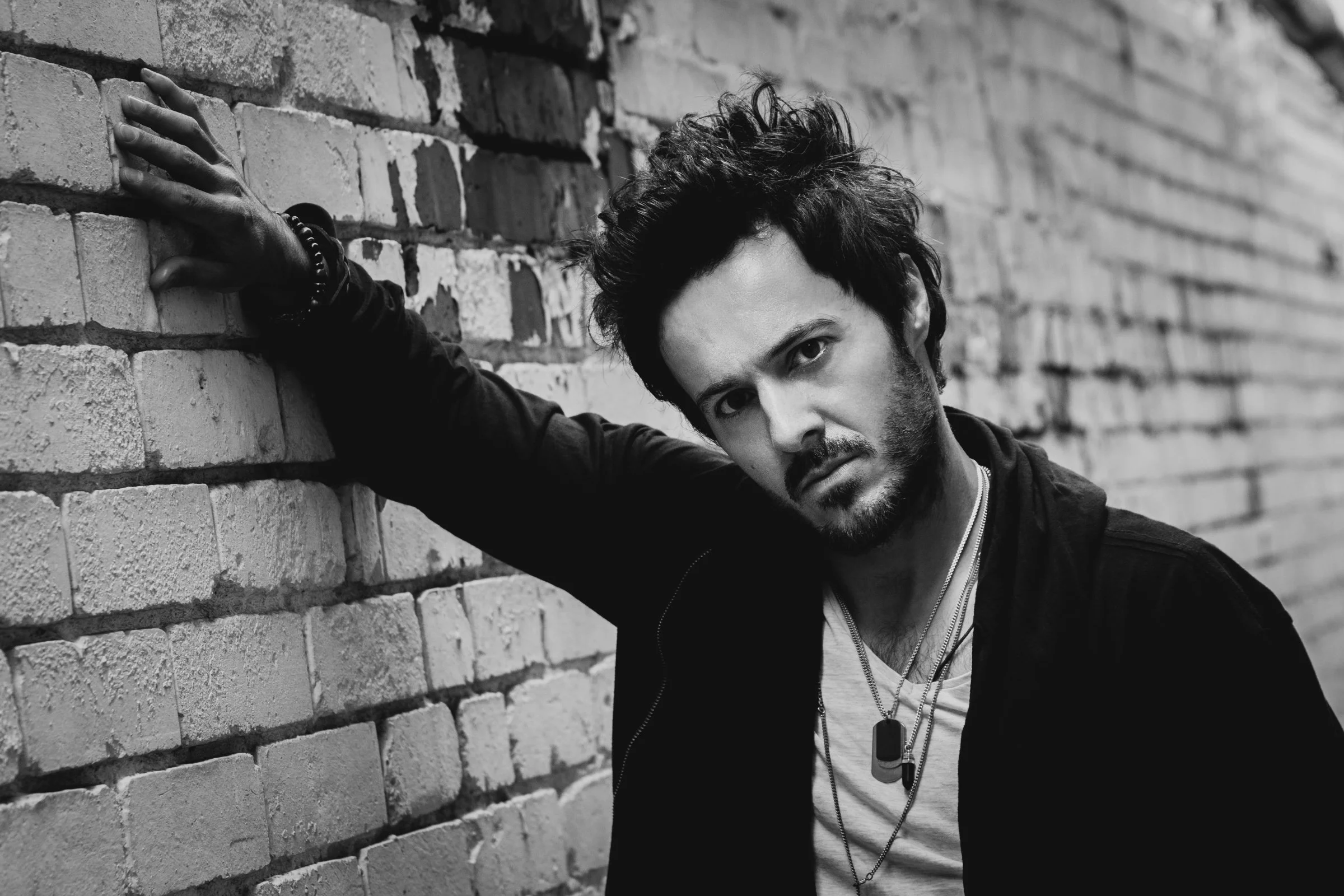 Musician, singer, author and podcaster, James Kennedy promo photo standing against a wall in black in white