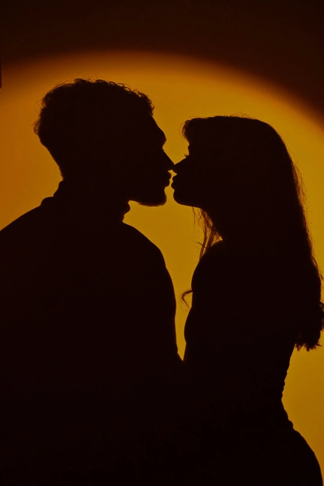 Silhouettes d'un homme et d'une femme se rapprochant pour s'embrasser, avec un fond de dégradé orange et jaune.