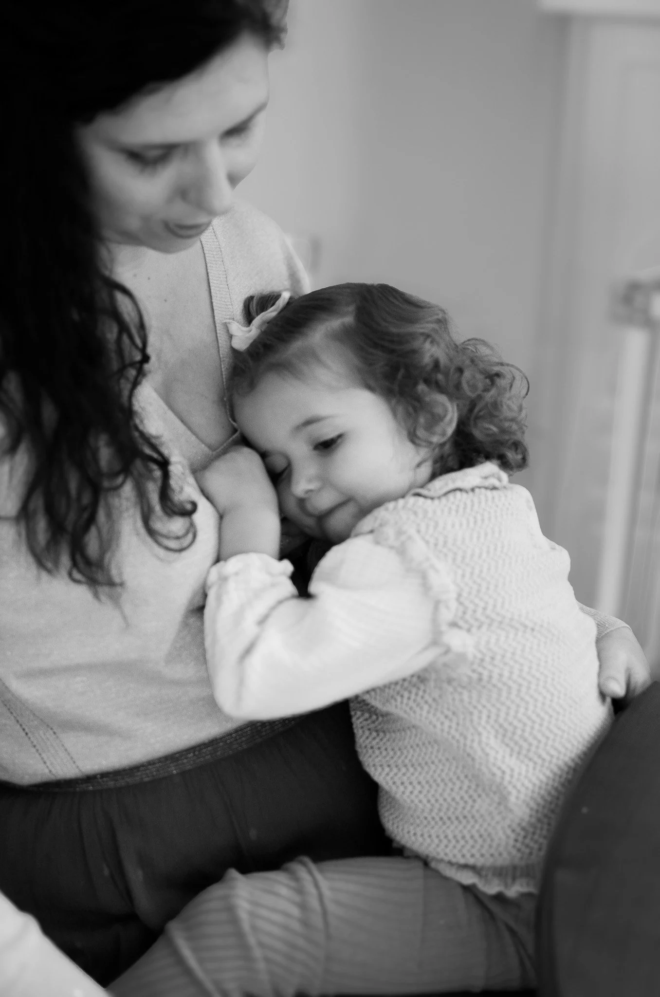 Une mère et sa fille partagent un moment affectueux dans un environnement intérieur, la fille repose sa tête contre la mère.