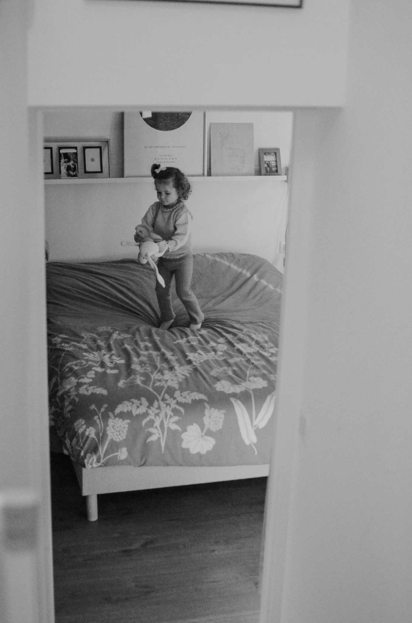 Une petite fille joue avec un jouet dans une chambre, vue à travers une ouverture dans un mur