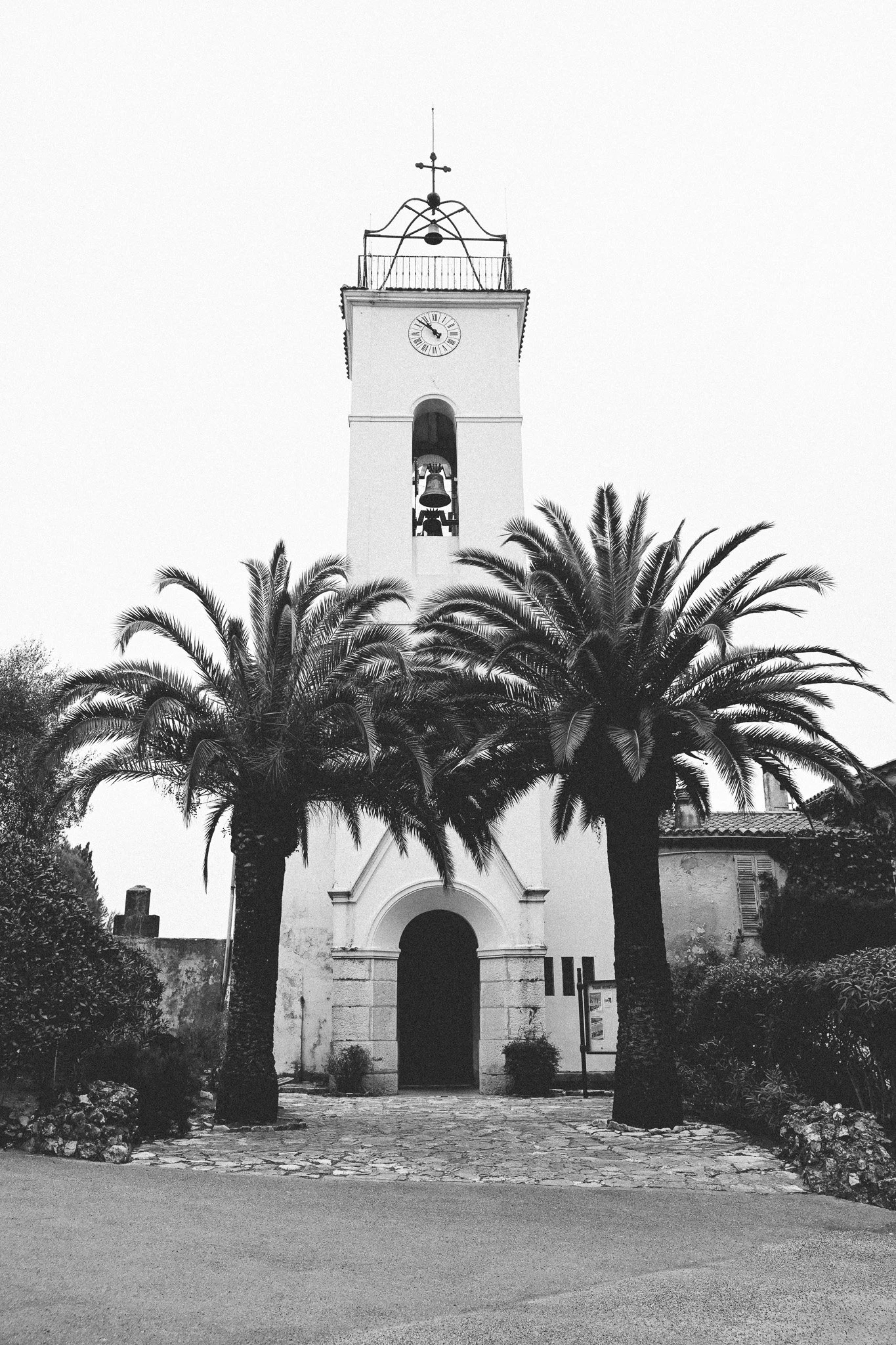 Une église blanche avec une horloge sur la façade, entourée de palmiers, vue en noir et blanc.