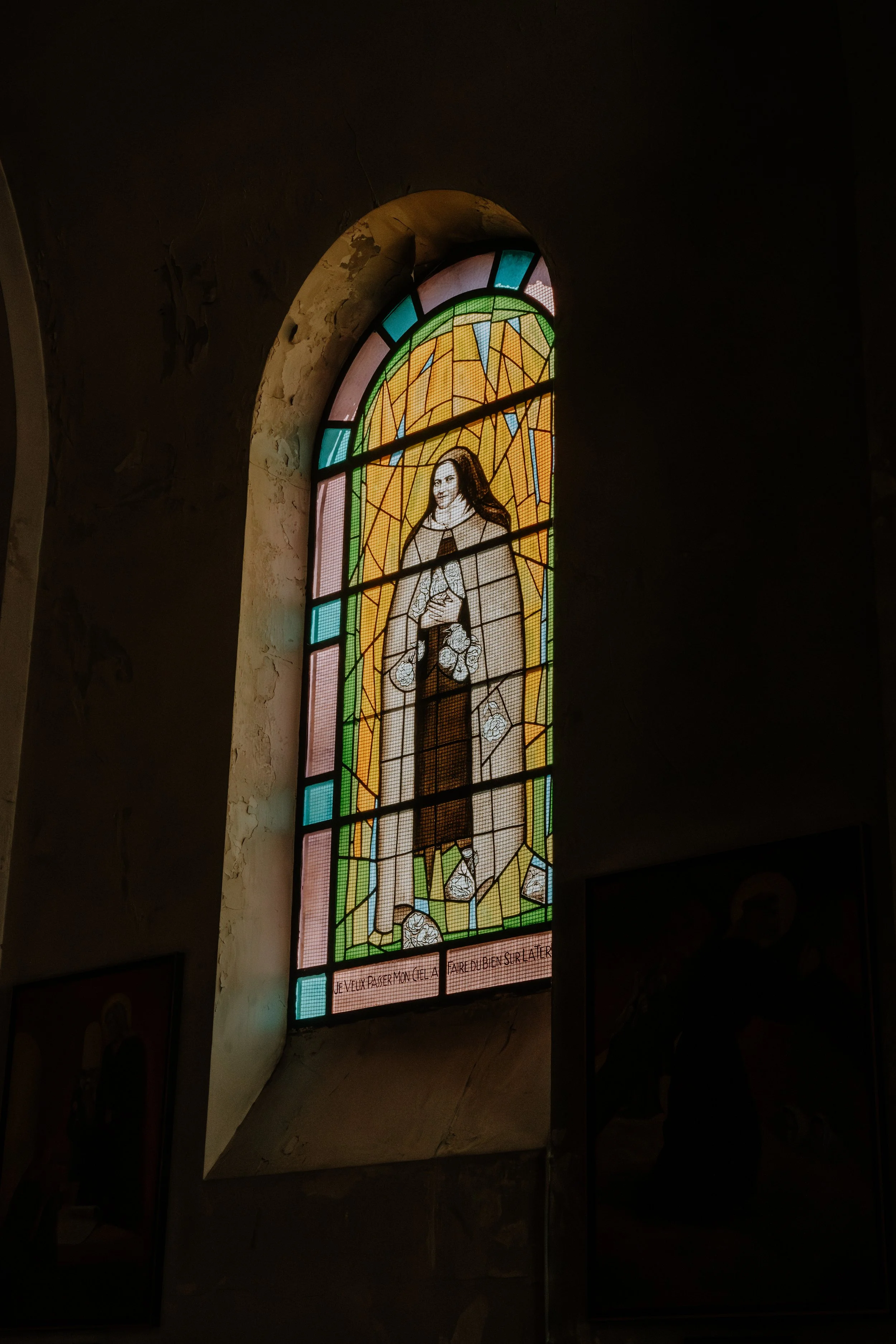 Vitrail représentant une femme avec un halo doré, tenant une croix avec des roses autour, avec une inscription en français en dessous.