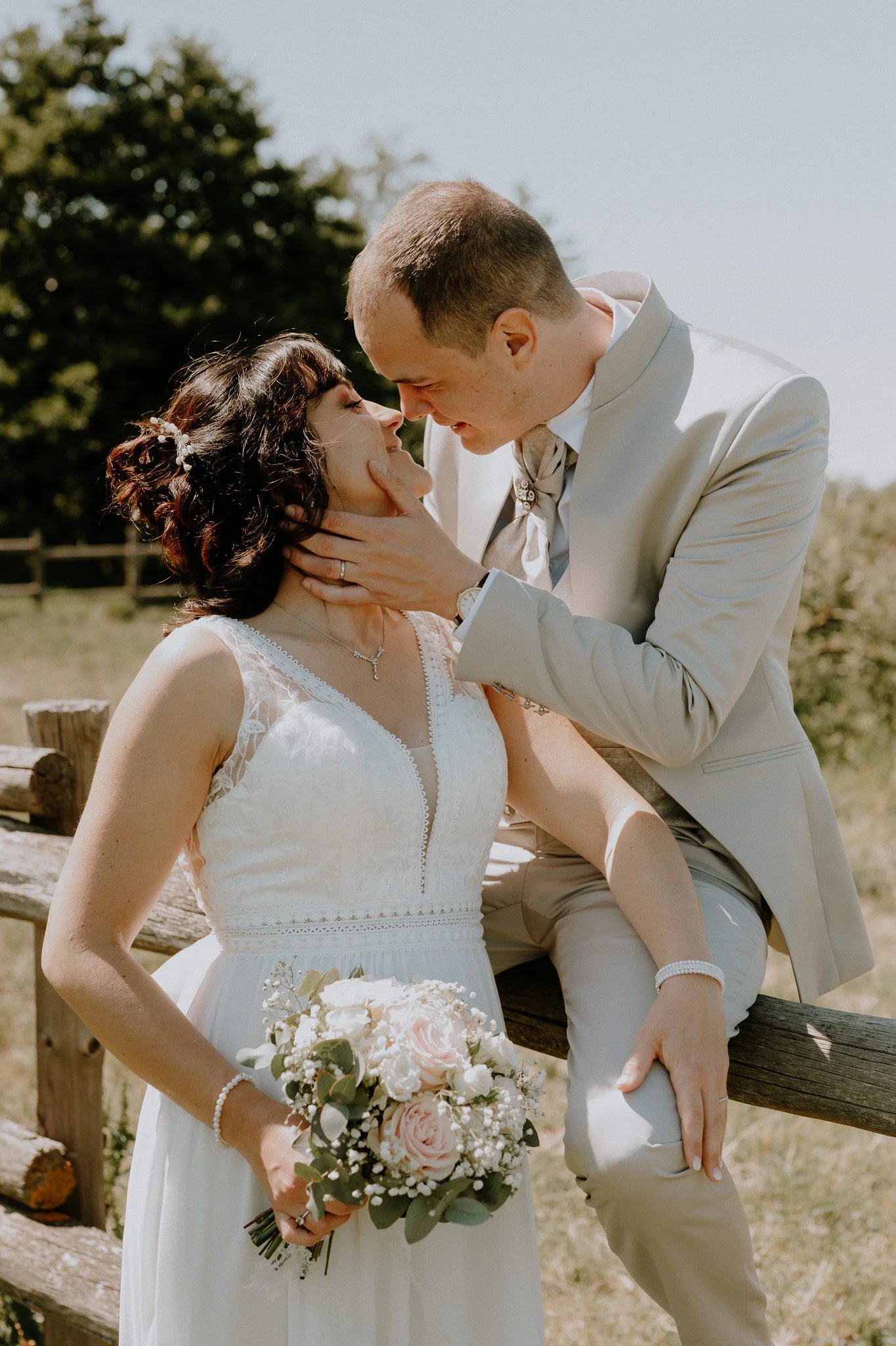 Un couple en mariage pose en extérieur, la femme en robe blanche et le homme en costume clair, lors d'une séance photo