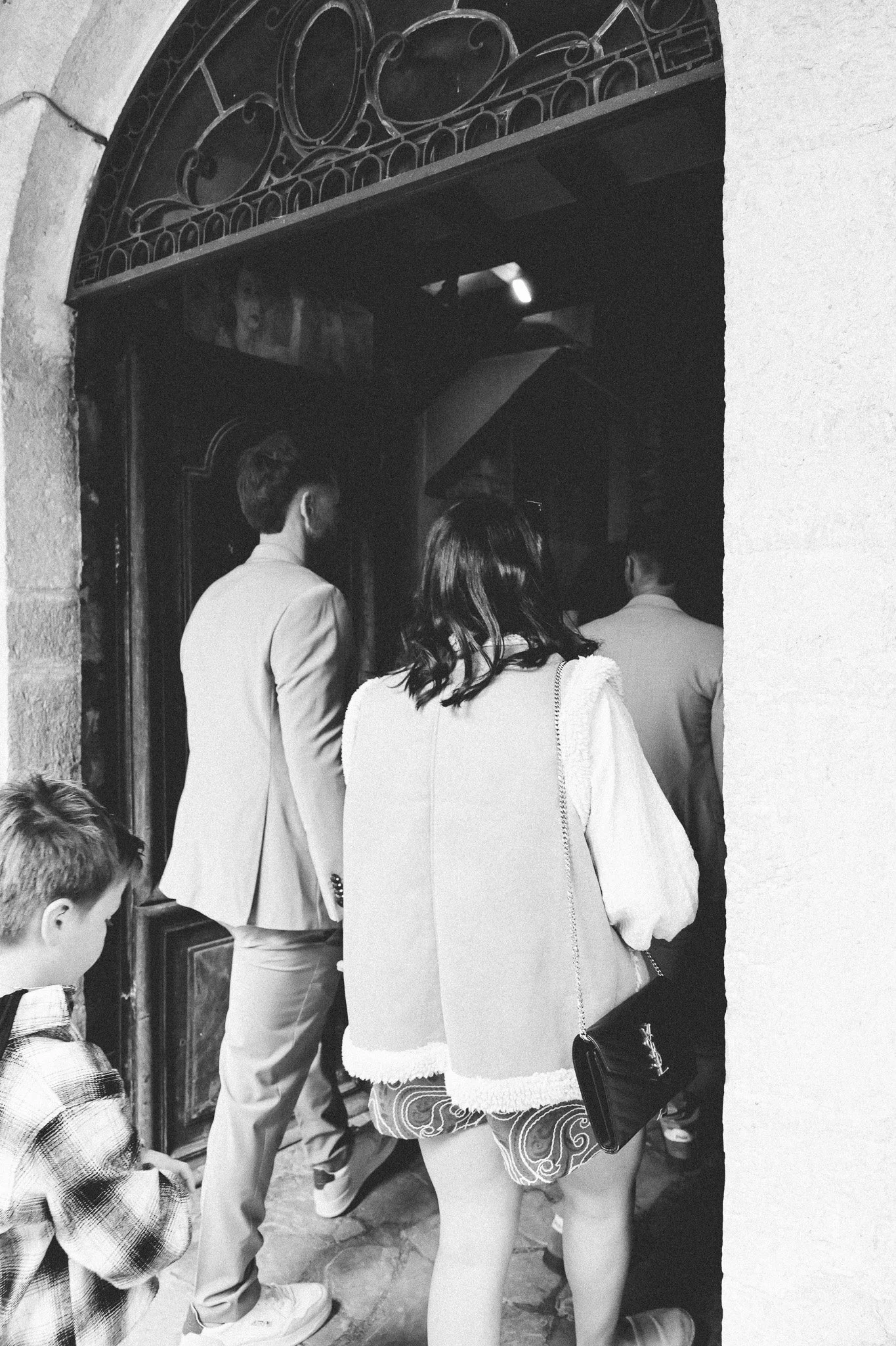 Groupe de personnes debout dans une entrée ou un couloir, en train d'attendre ou de faire la queue, dans un bâtiment historique ou religieux.