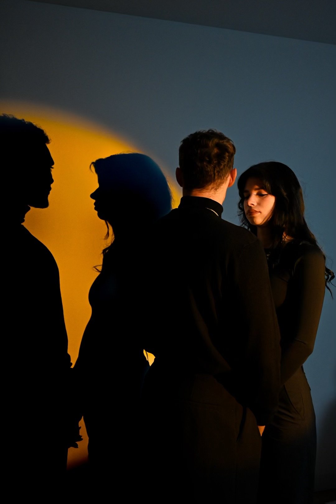 Groupe de quatre personnes, deux hommes et deux femmes, discutant dans un studio avec un fond bleu. Les silhouettes sont en partie en ombre, avec un éclairage diffus créant un effet de silhouettes et d'ombres colorées.