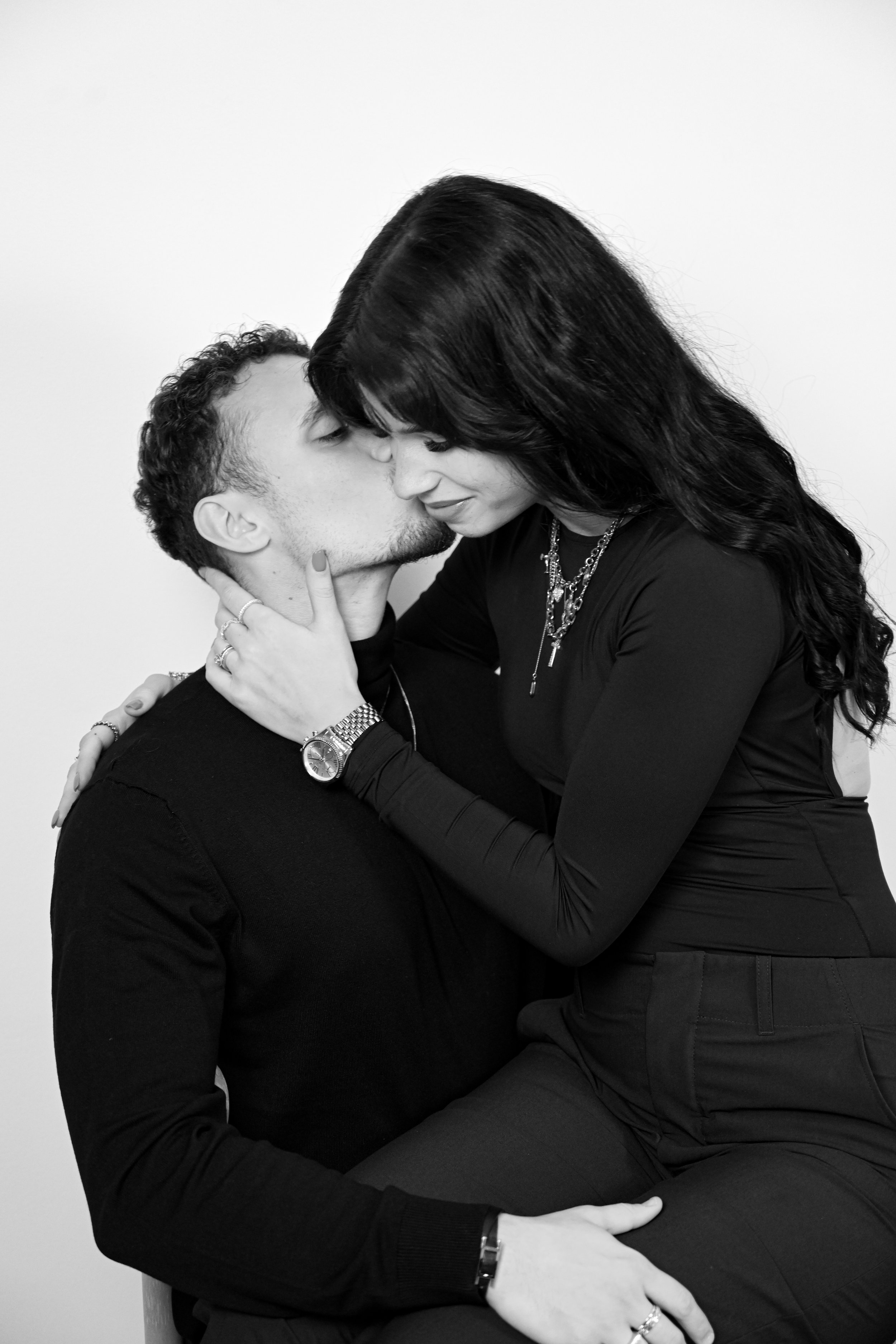Un homme et une femme s'embrassent dans une pose intime. La femme porte plusieurs colliers et des bijoux, et l'homme porte une montre.
