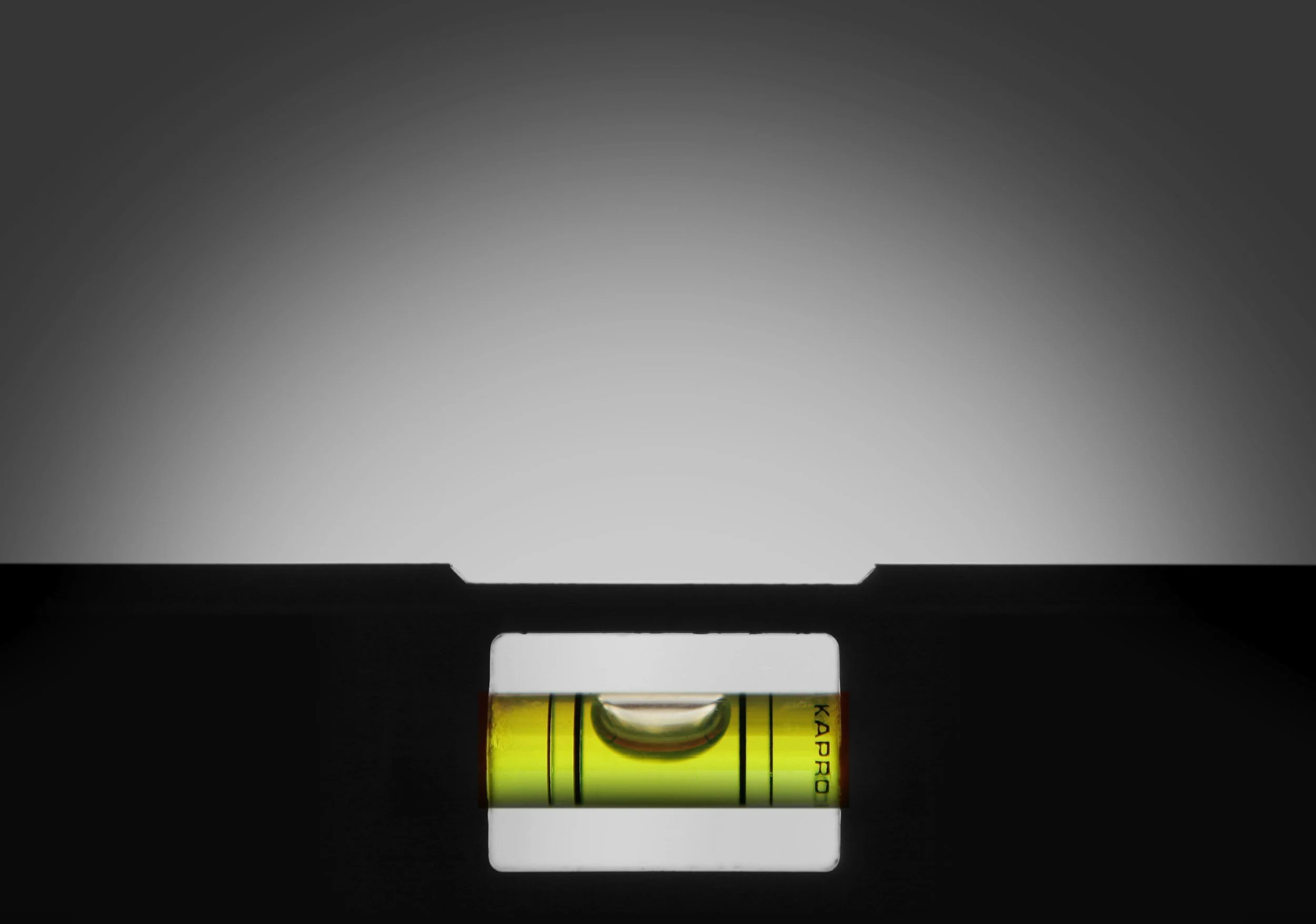 Close-up of a yellow spirit level tool with a bubble, positioned on a flat dark surface, with a blurred gradient gray background.