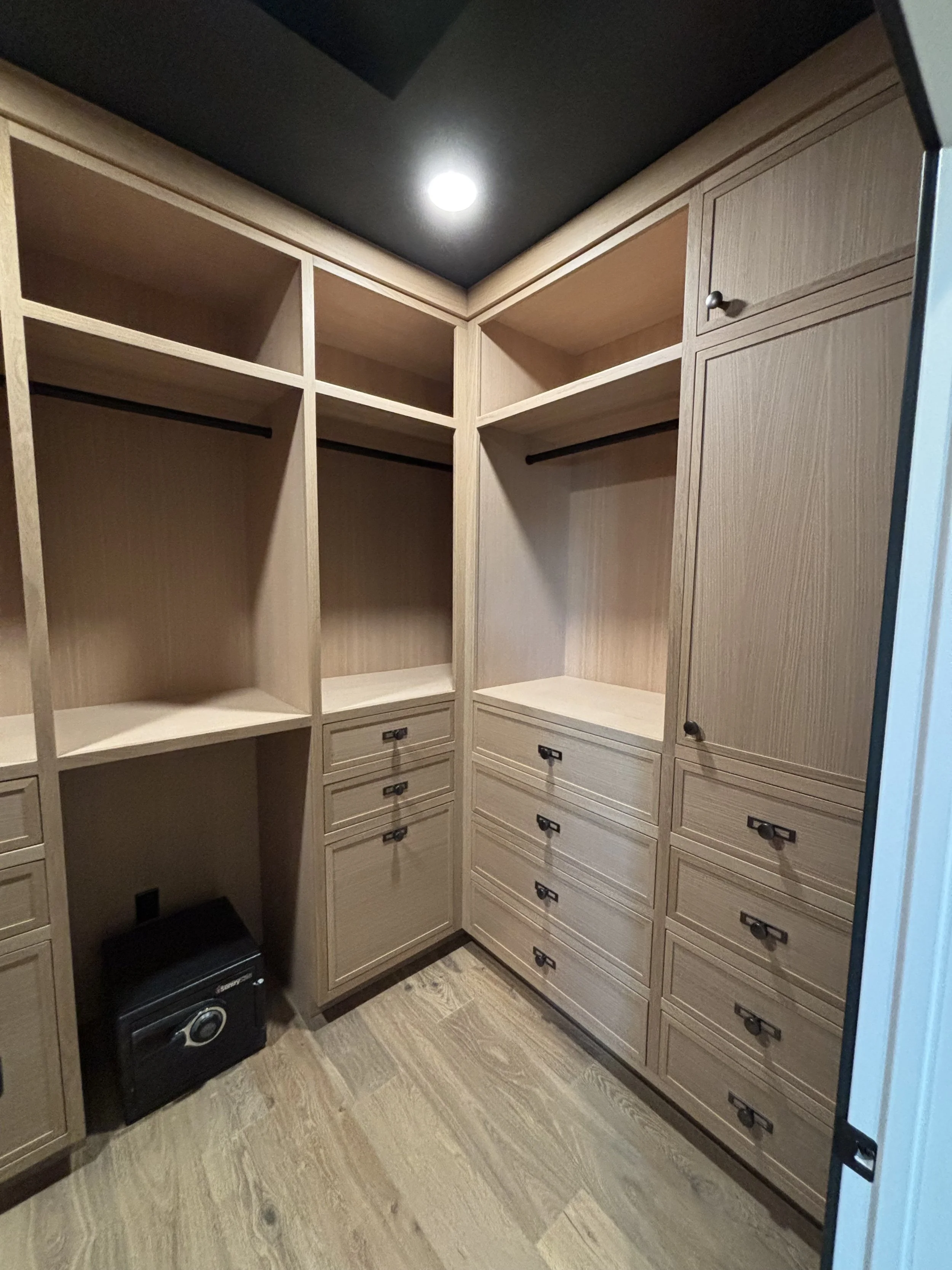 Empty walk-in closet with built-in wooden shelves and drawers, and a small safe on the floor.