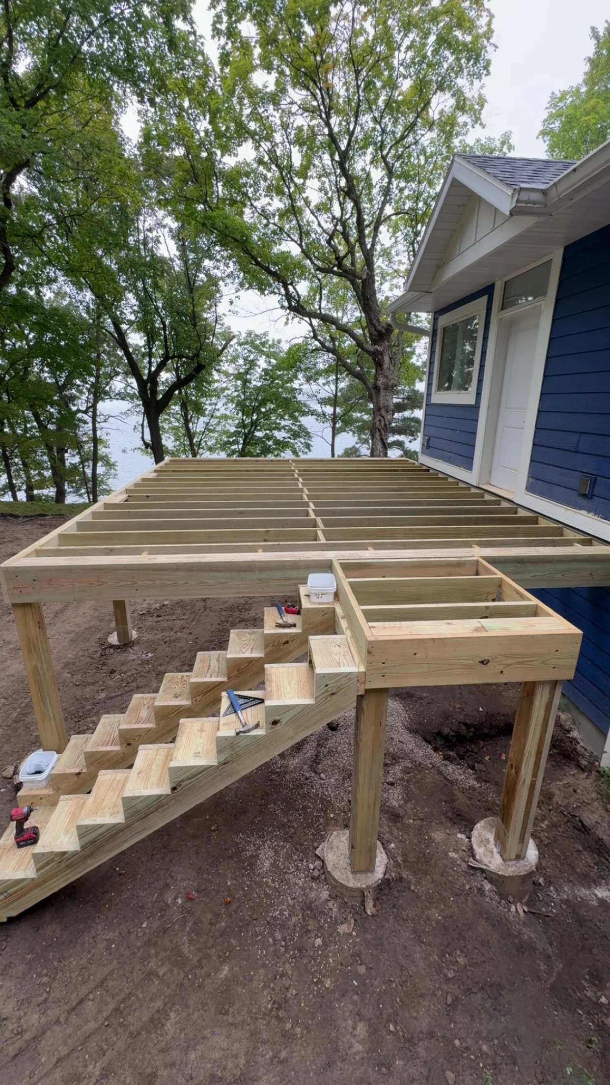 Wooden staircase under construction outside a blue house with trees in the background.
