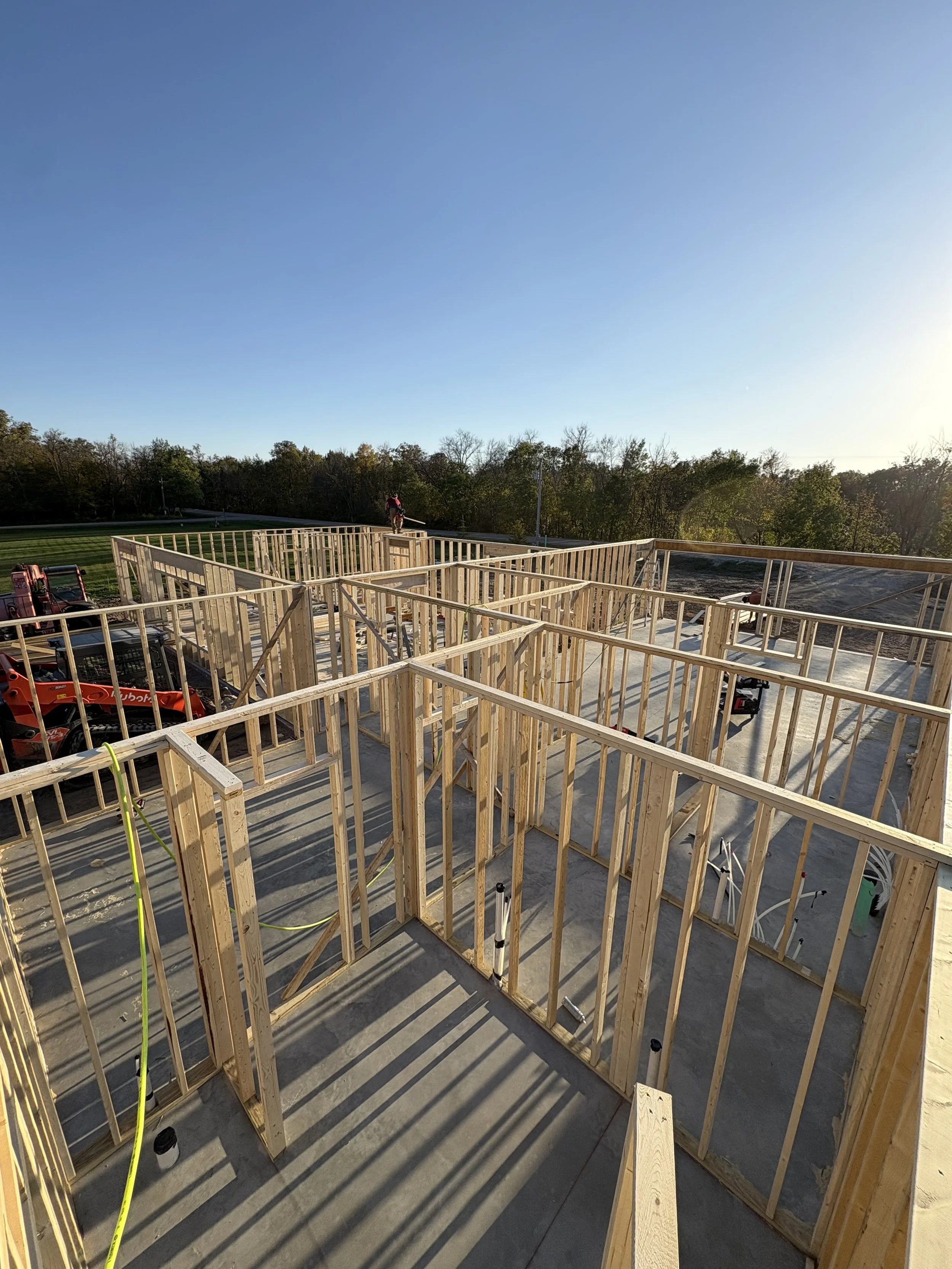 Wooden framing for a building under construction with a clear sky and trees in the background.