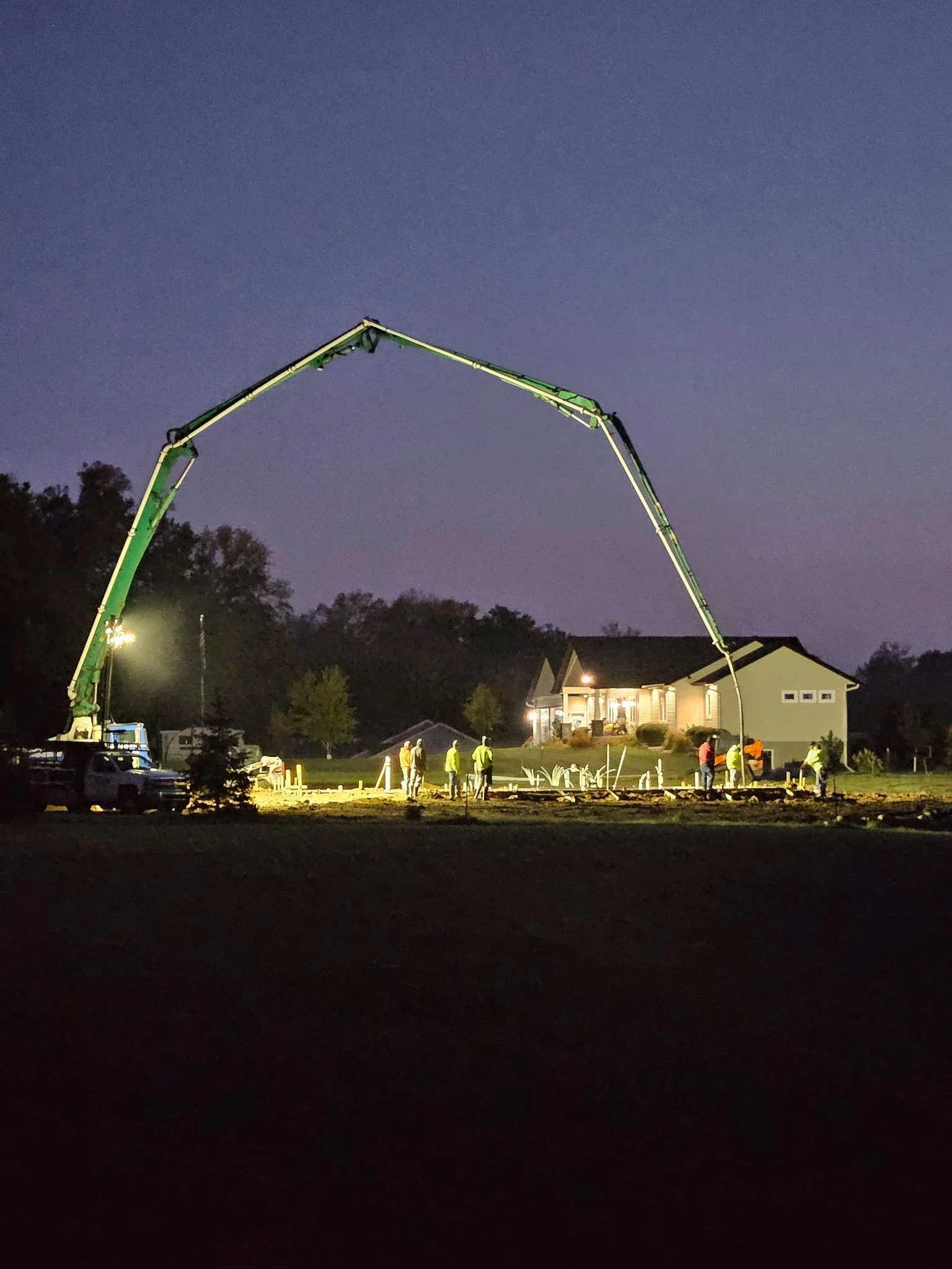 Construction workers operating heavy machinery at night on residential site.