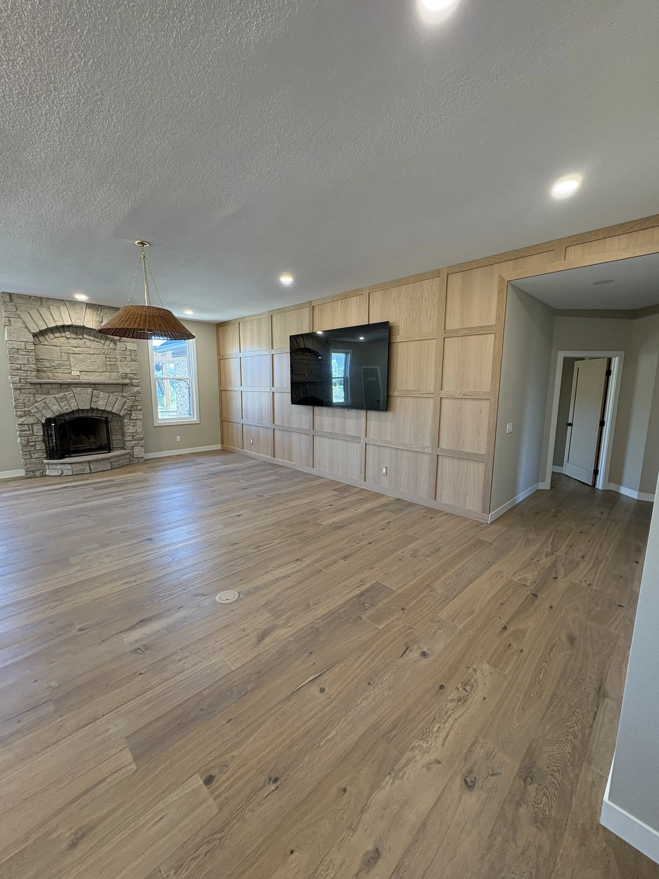Living room with wooden flooring, a stone fireplace, a mounted flat screen TV, and light-colored walls.