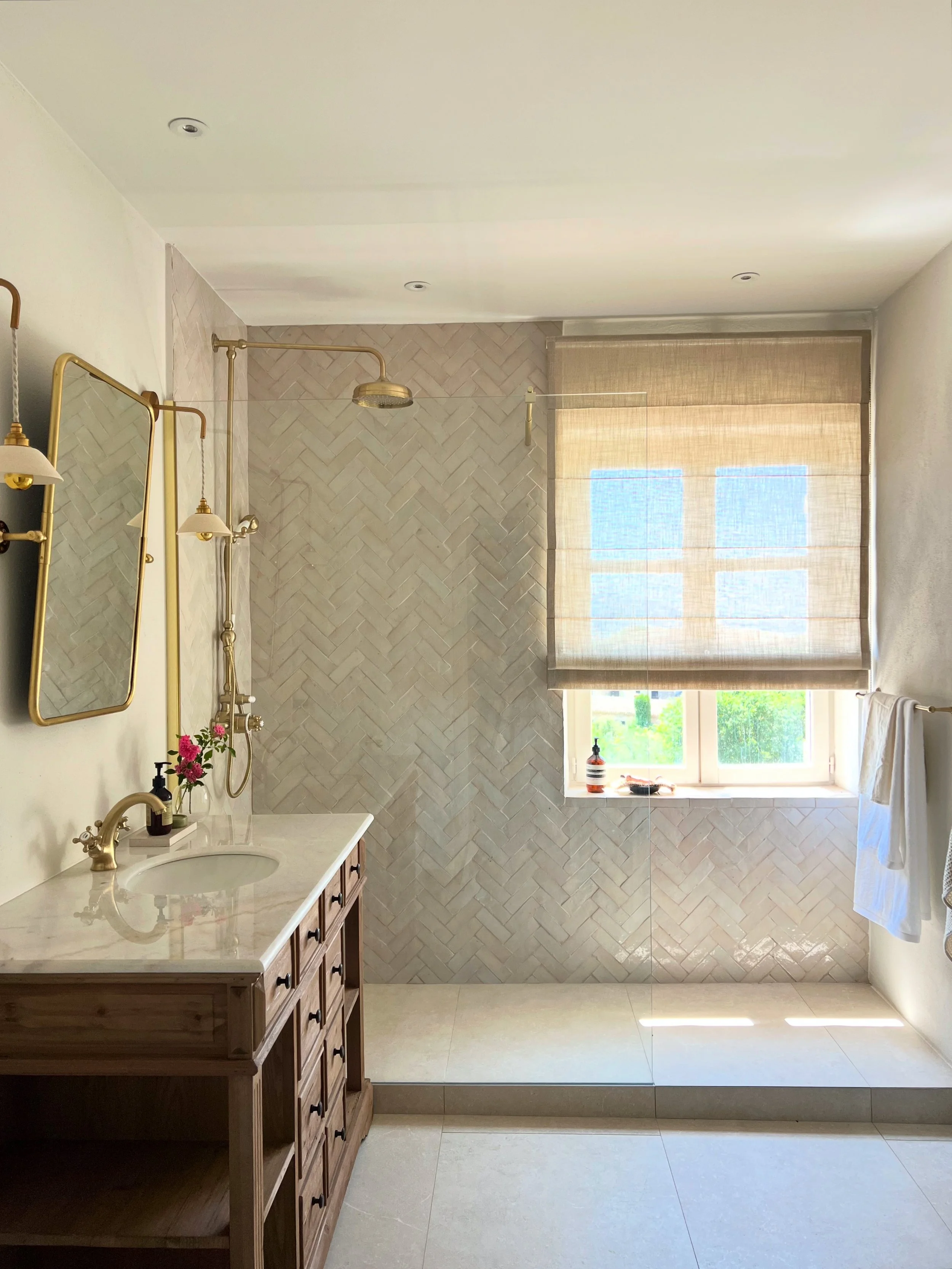 shower tiled in zellige bejmat handmade tiles, herringbone, brass taps and shower, sheer linen blinds, soft white towels, luxury bathroom, wellness, antique vanity, marble, stone, mirror, enamoura lights, light, sun light, Aesop