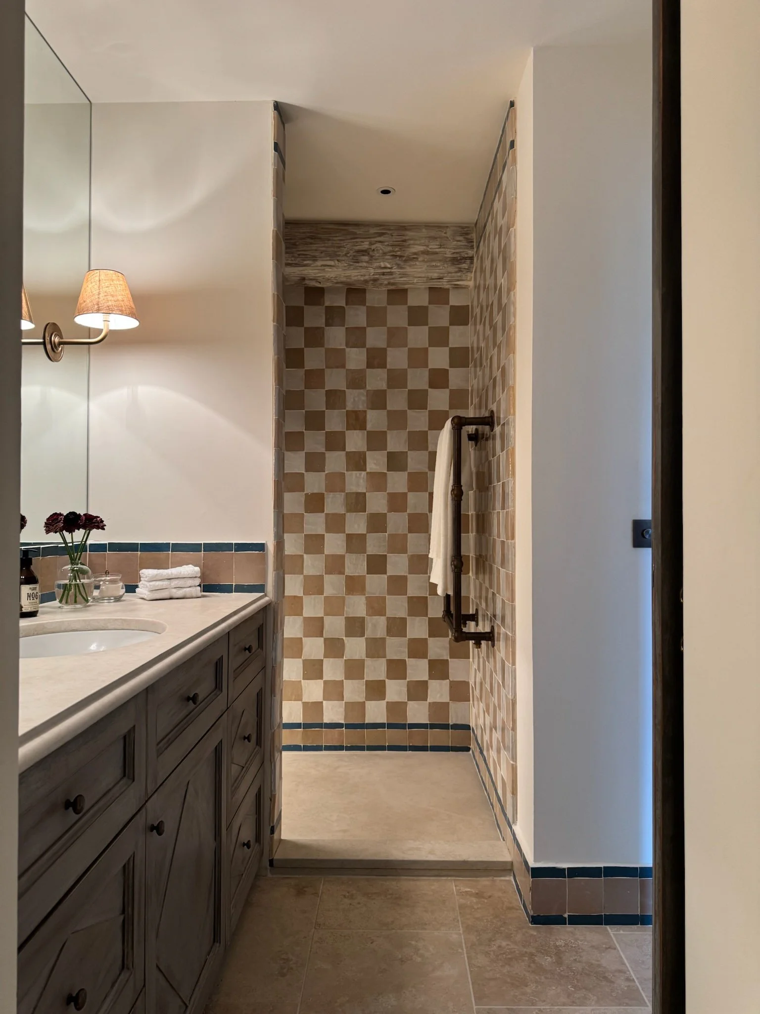 Bathroom with a vanity, mirror, and a walk-in shower with beige checkered tiles, rustic metal towel rack, and neutral-colored tiled floor.