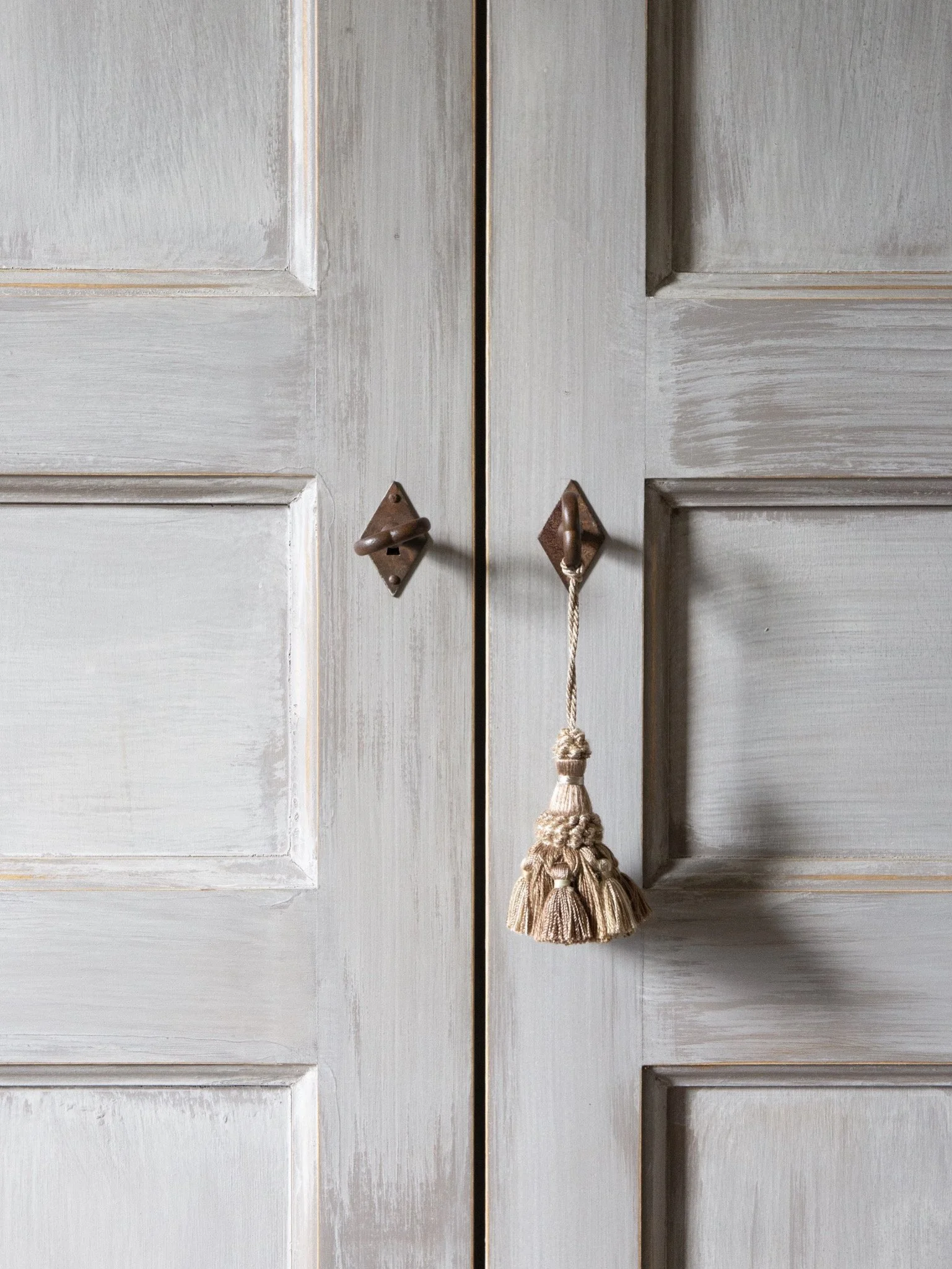 Close-up of white wooden wardrobe doors with brass handles, one handle has a cream tassel hanging from it.