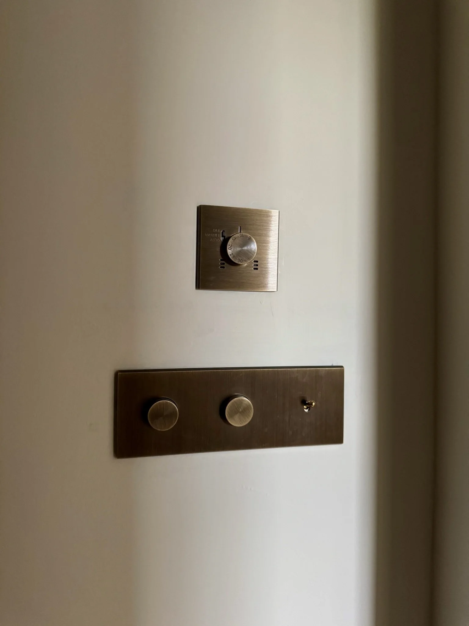 Close-up of a wall with a thermostat and a metal control panel with two knobs.