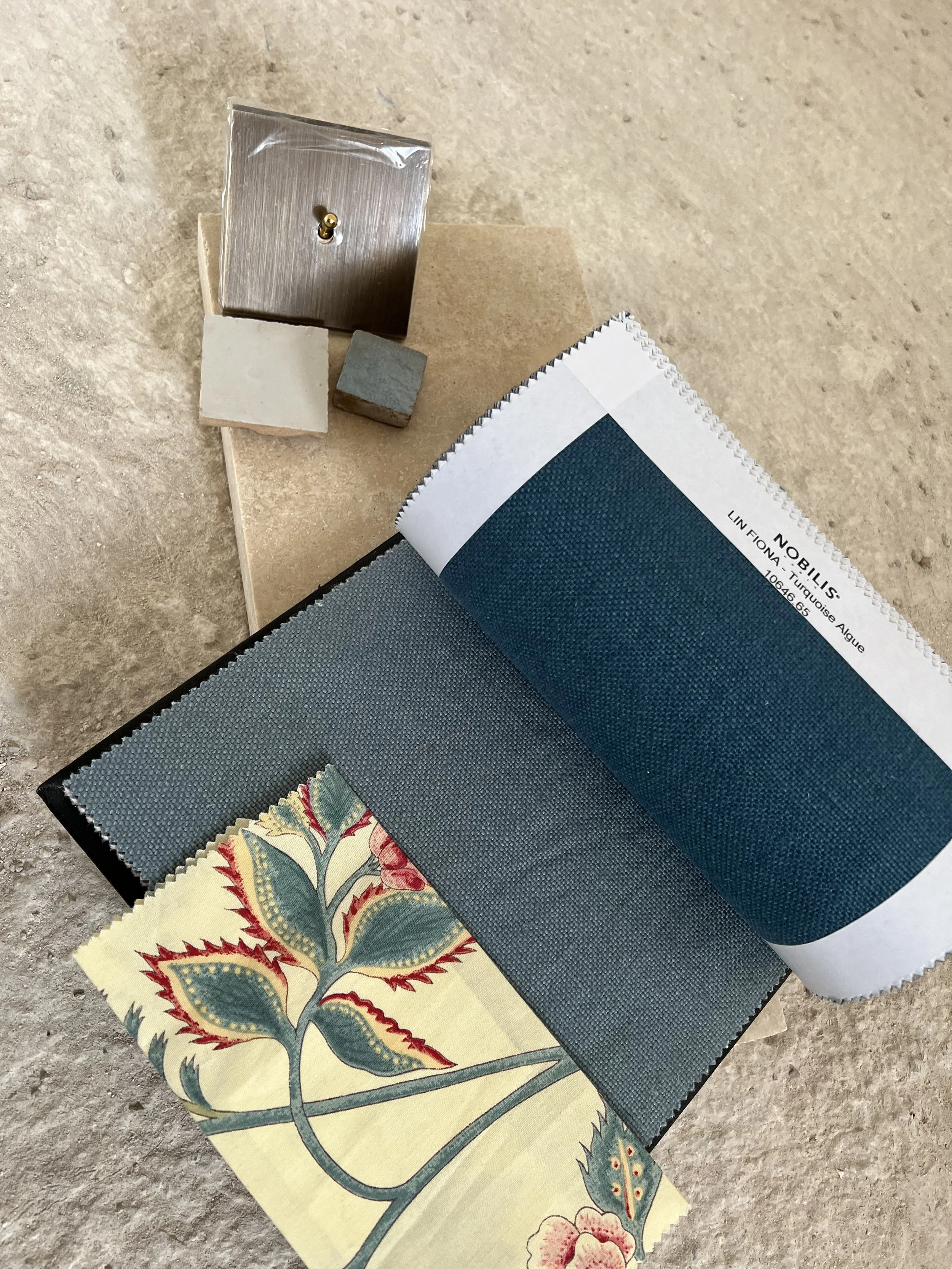 A collection of fabric sample swatches, a color palette book, small tiles, and a metal fixture on a rough surface.
