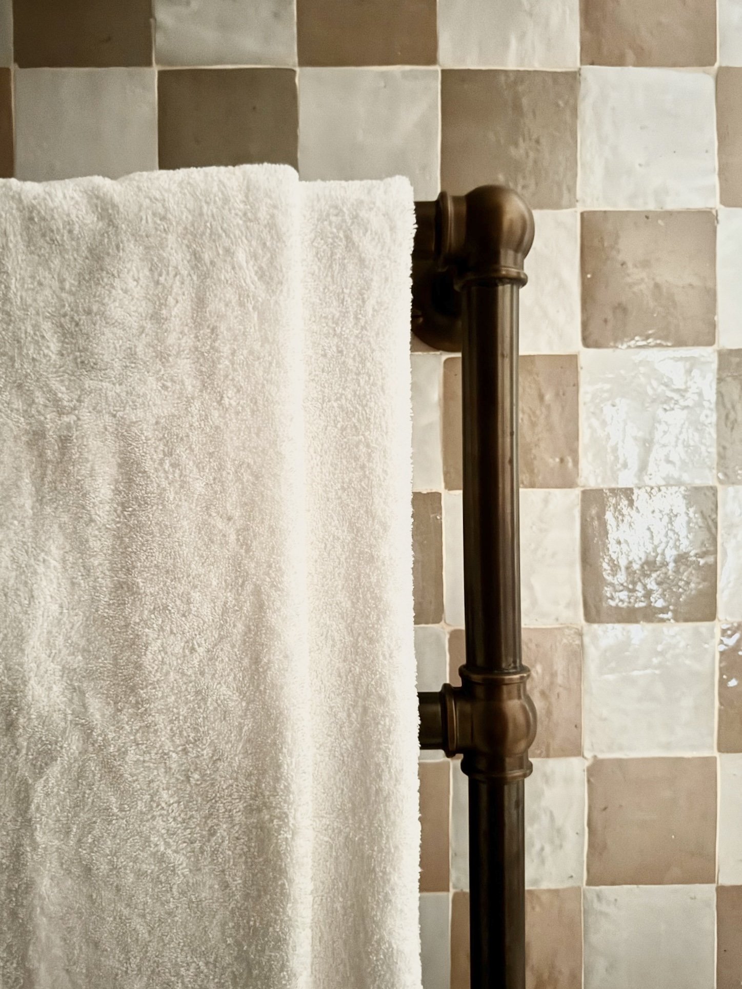 Close-up of a brass bedpost with a white towel draped over it, with tiles in beige and cream shades in the background.