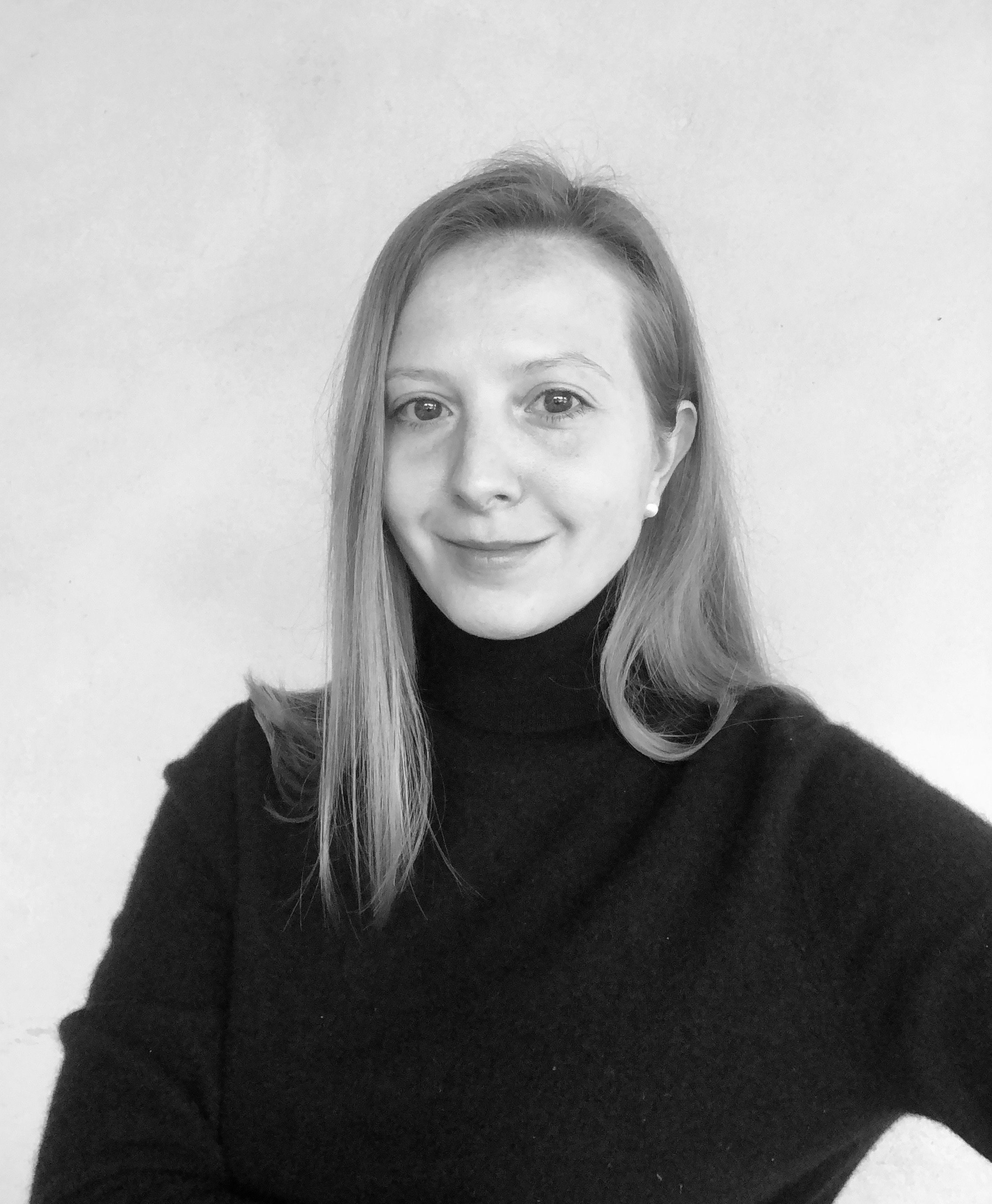 Black and white portrait of a young woman with light skin, long straight hair, wearing a black turtleneck, smiling at the camera against a plain light background.
