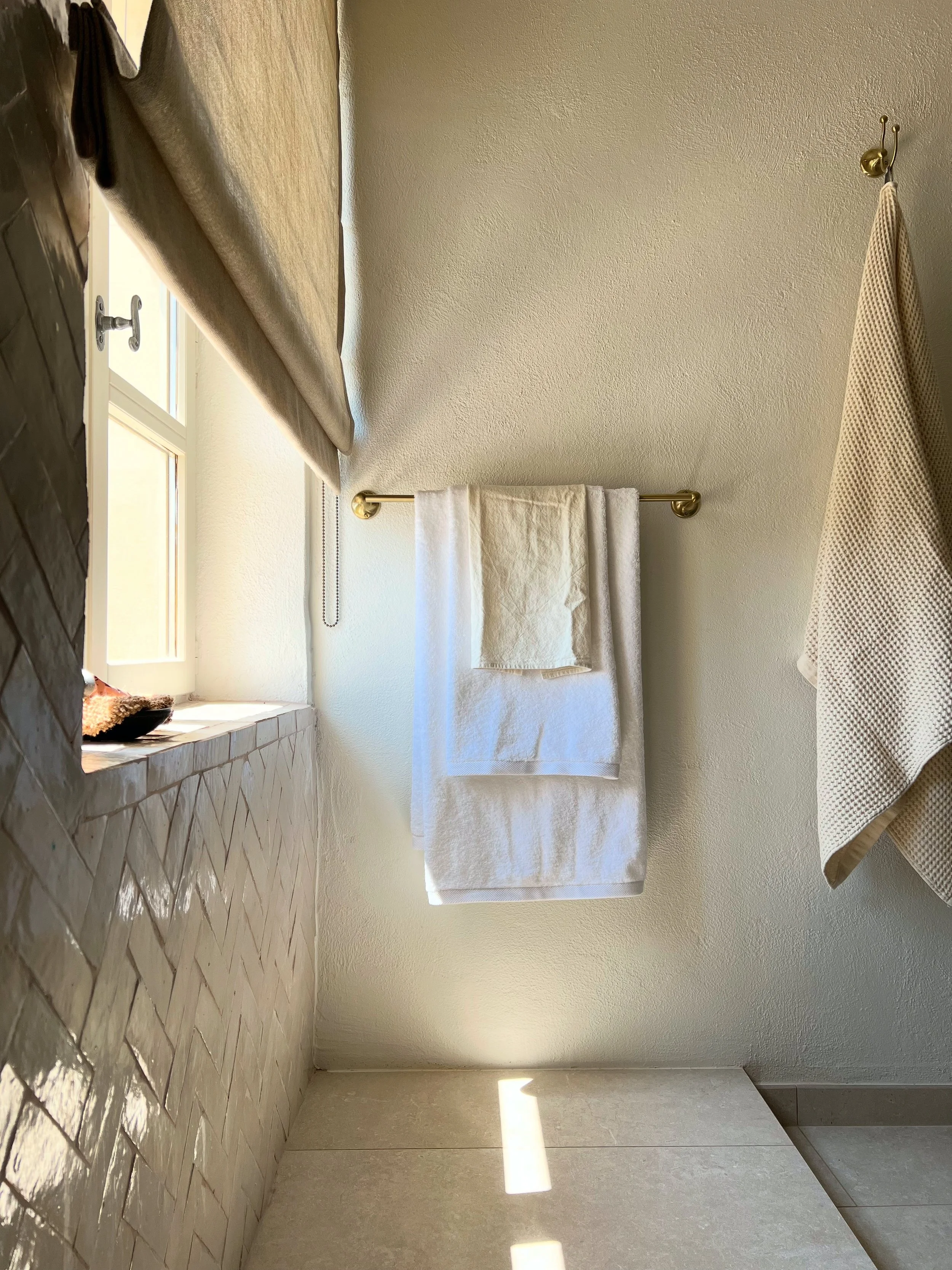 shower tiled in zellige bejmat handmade tiles, herringbone, brass taps and shower, sheer linen blinds, soft white towels, luxury bathroom, wellness, light, sun light, sanctuary