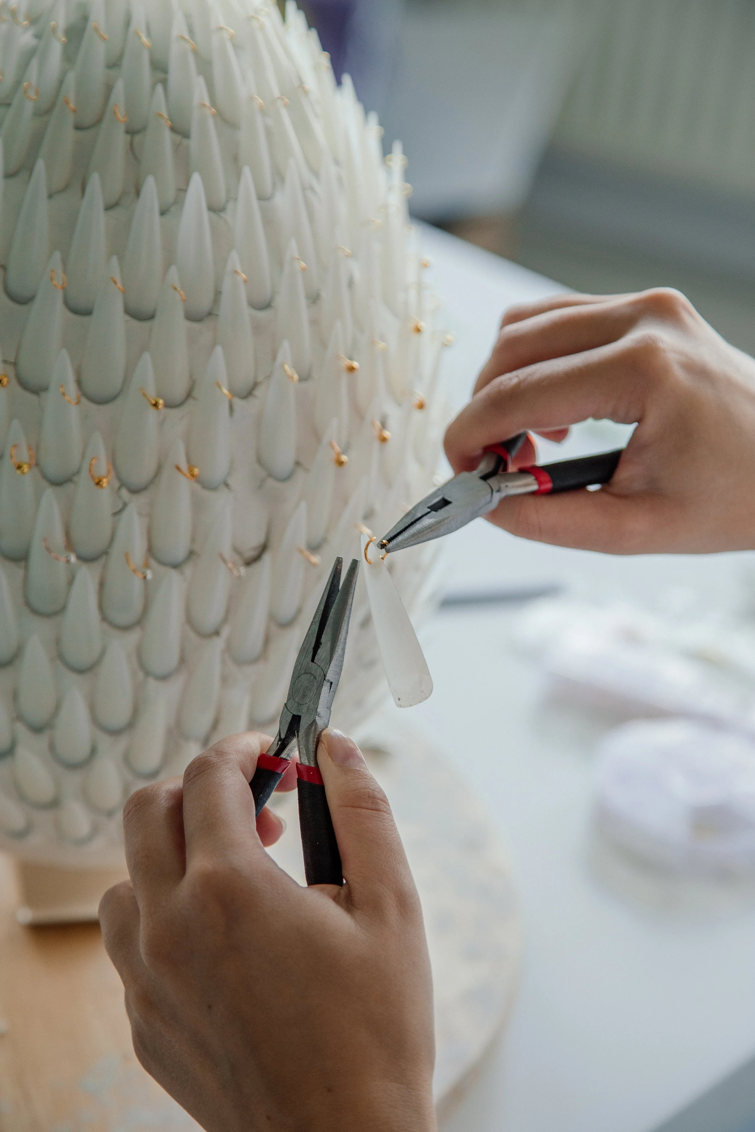 Person using pliers to attach gold hooks to white ceramic cones on an art sculpture.