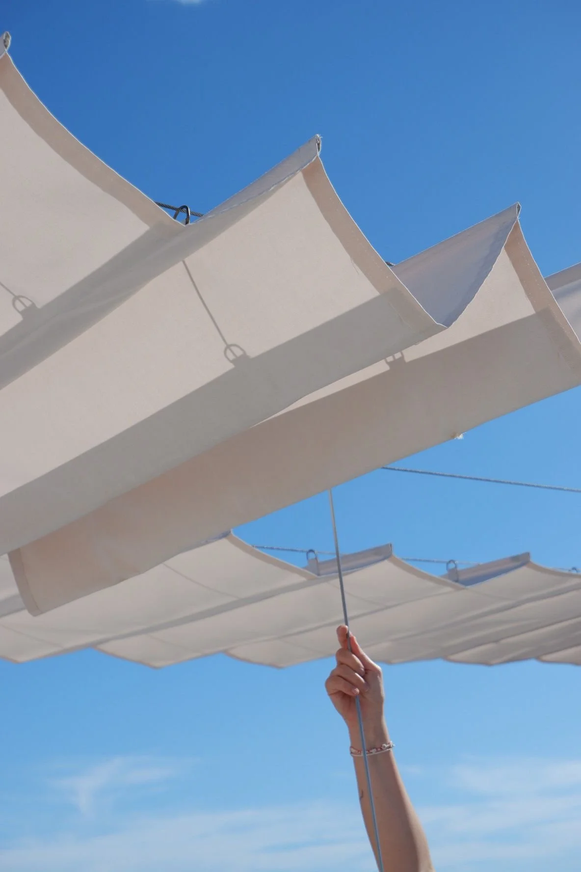 Person holding a string under white beach umbrellas against a clear blue sky.