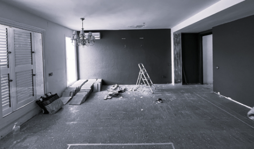 Empty room under renovation with a chandelier, ladder, and construction debris.
