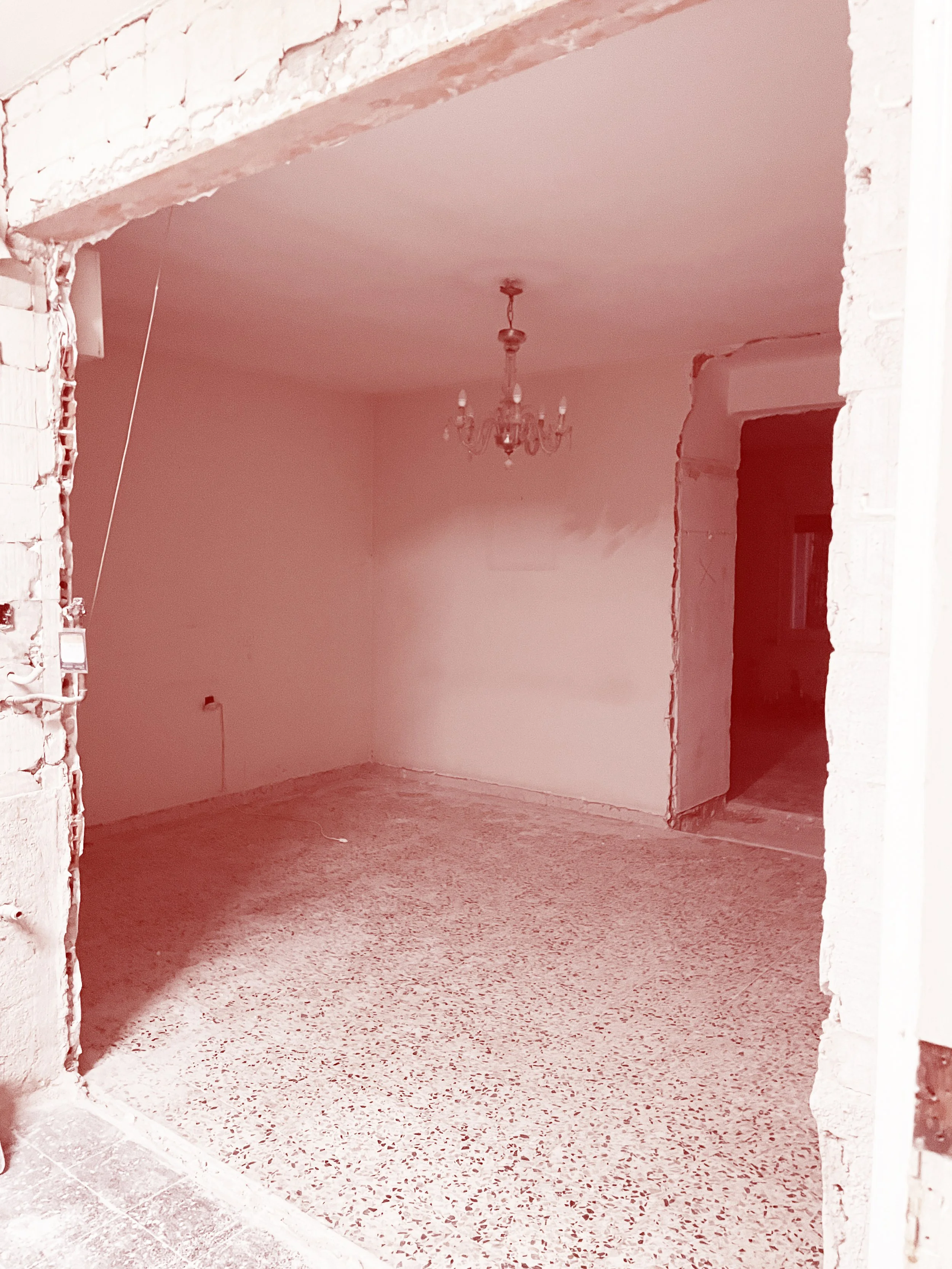 Unfinished interior room under construction with a chandelier hanging from the ceiling, exposed brickwork around the doorway, and a terrazzo floor.