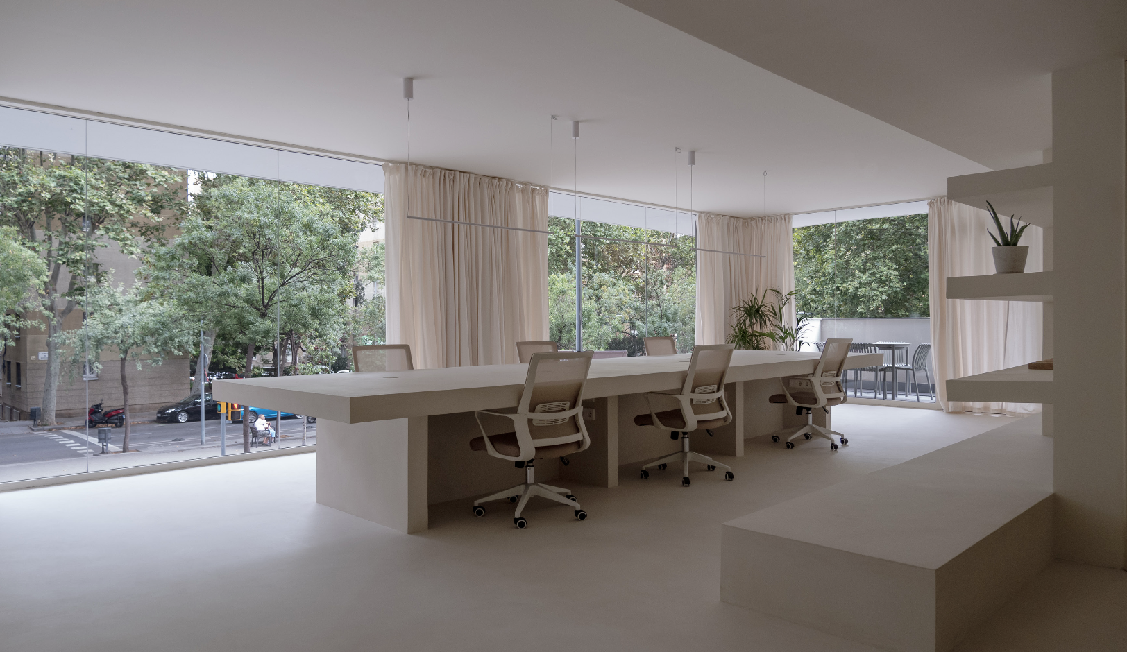 Modern conference room with a long white table, white chairs, and large windows with beige curtains. Outside, trees and city street are visible.