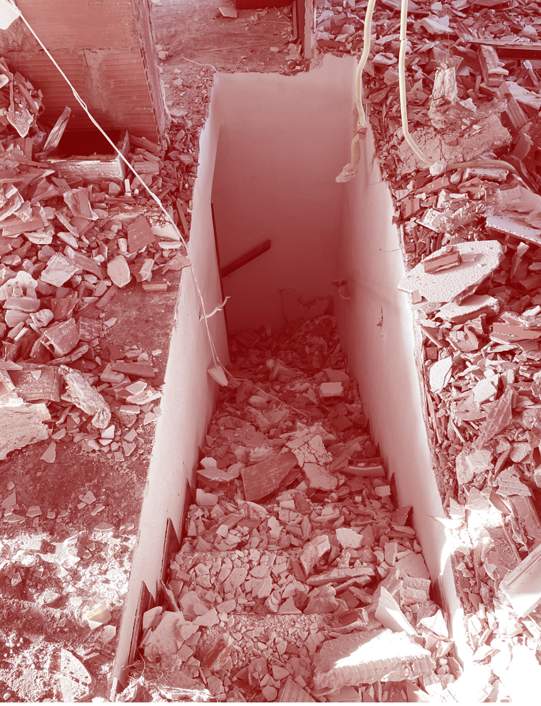 A staircase leading down to a basement or cellar, with debris and broken drywall scattered around and on the stairs, indicating ongoing demolition or construction.