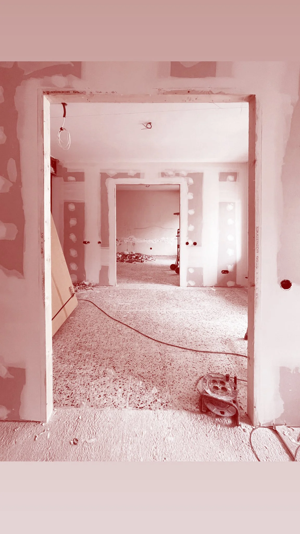 Interior view of a building under construction with drywall installation, exposed wiring, and unfinished walls.