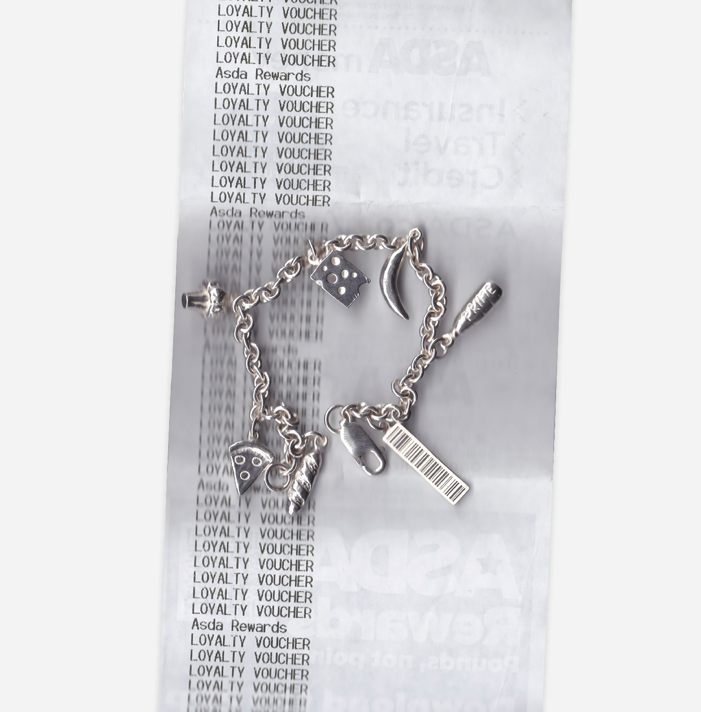 Silver charm bracelet with various charms, including a dice, moon, pizza slice, barcode, carrot, and a nail, placed on a receipt for Asda Rewards loyalty vouchers.