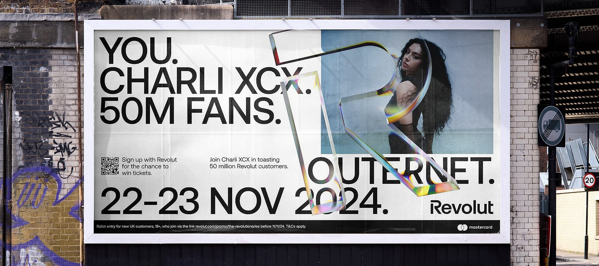 A billboard advertisement for Revolut featuring a woman with long curly black hair posing with her arms crossed. The text on the billboard says, "You. Charli XCX. 50M Fans. OUTERNET. 22-23 Nov 2024." There is a QR code and information about signing u