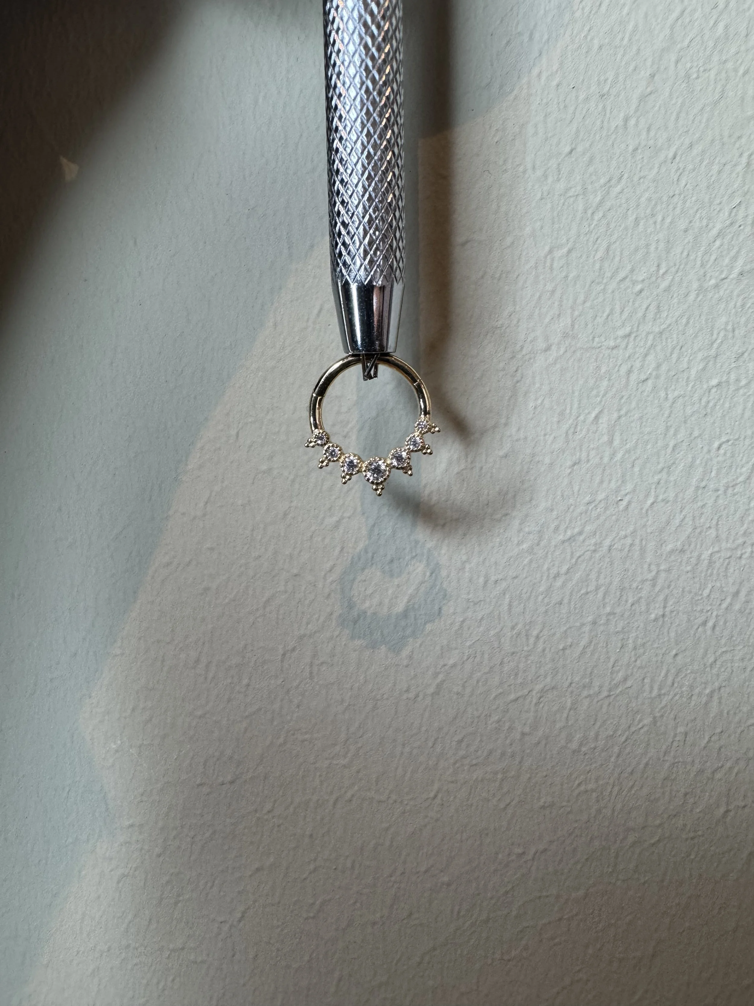 A silver hoop earring hanging from a textured metallic tool, casting a shadow on a beige wall.