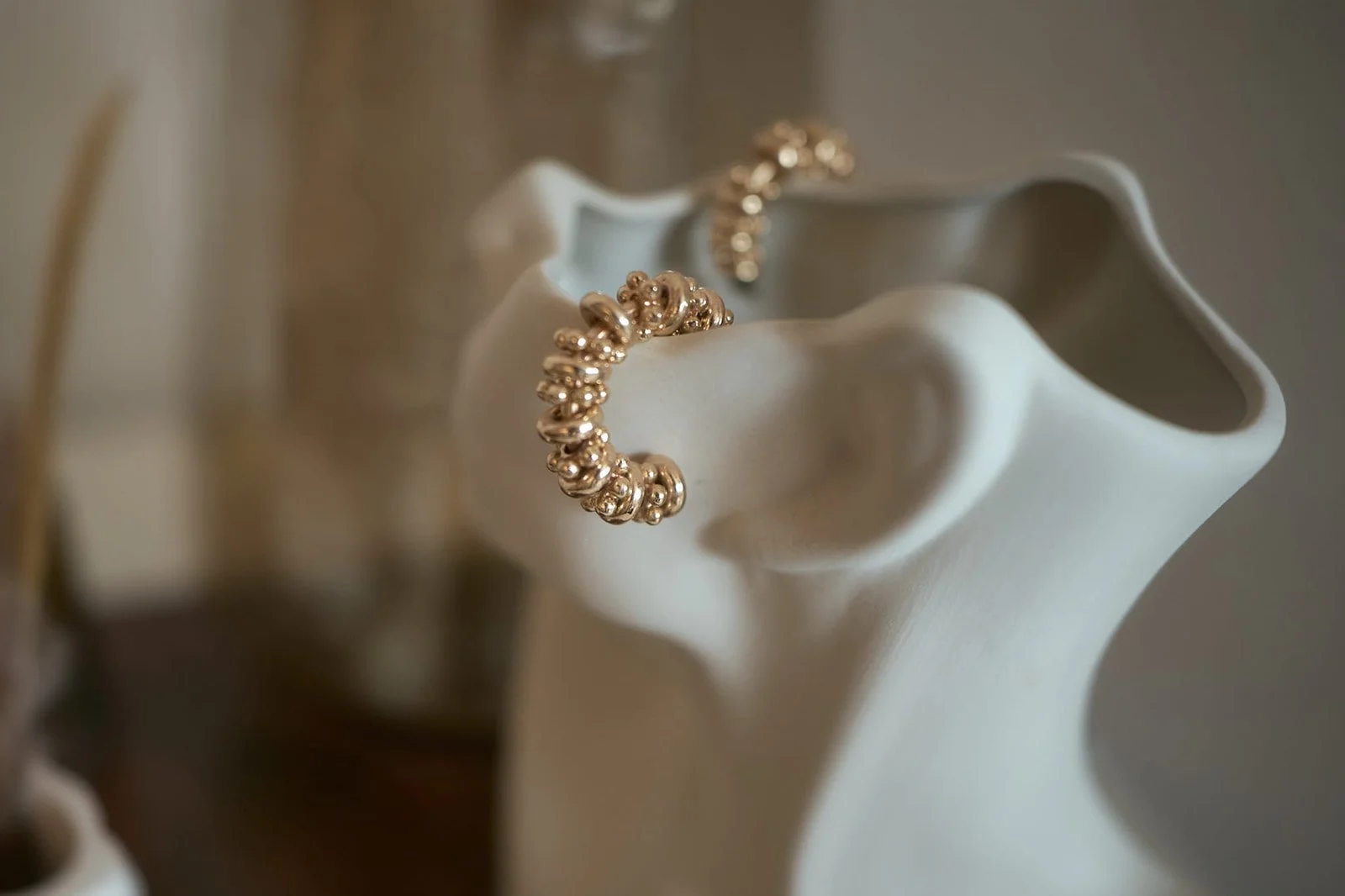 A close-up of a white ceramic or porcelain vase with a gold bracelet draped around its opening.