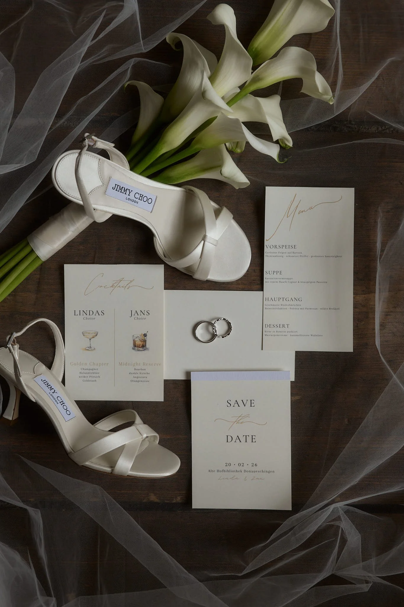 Wedding planning flat lay with white heels, calla lilies, rings, and wedding invitations.