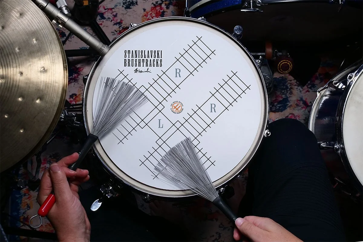 A special pad for brushes, lying on a snare drum, with visible train tracks indicating the lateral movement of the brush