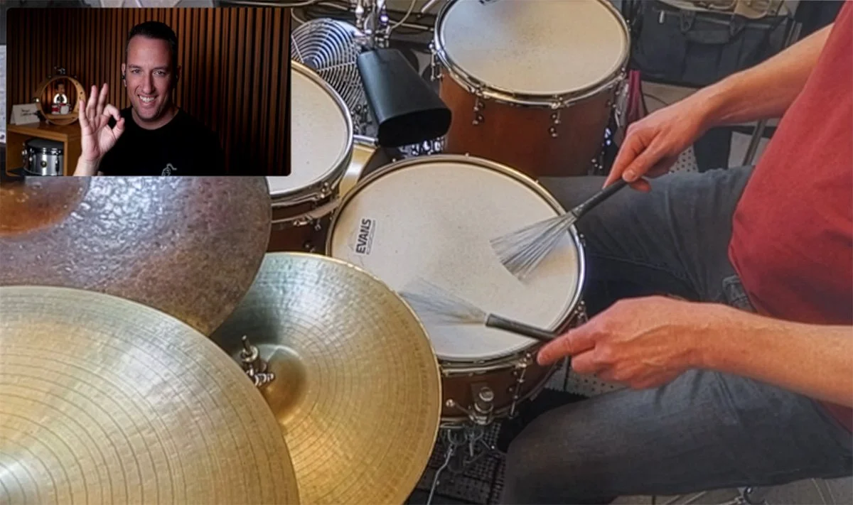 A person playing a drum set with various drums and cymbals, while another person is seen on a video call or recording, making an OK hand gesture.