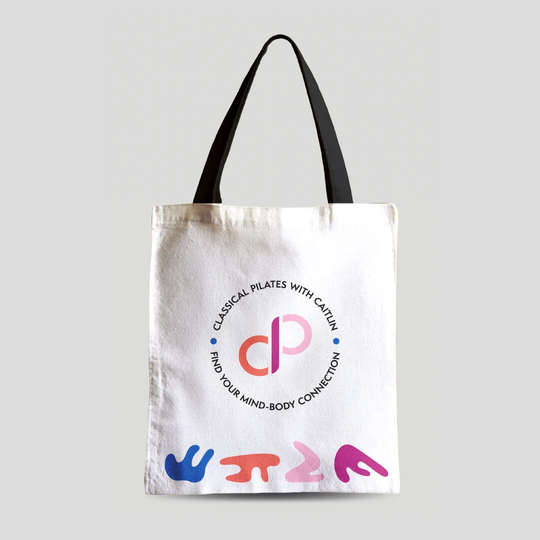 A mockup of a "Classical Pilates with Caitlin" tote bag, featuring four colorful blobs at the bottom.
