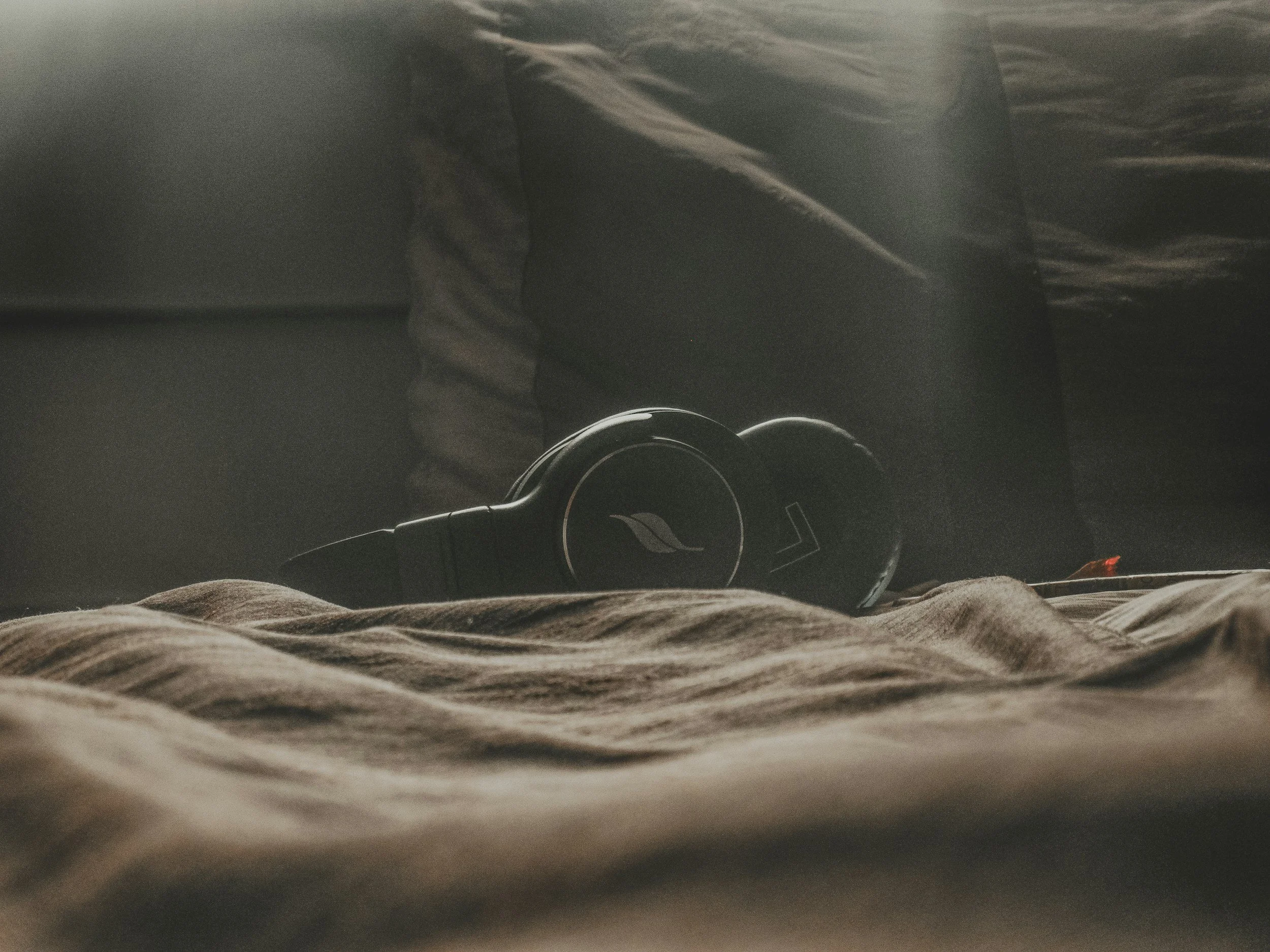 A pair of headphones resting on a rumpled fabric surface with a dark background.