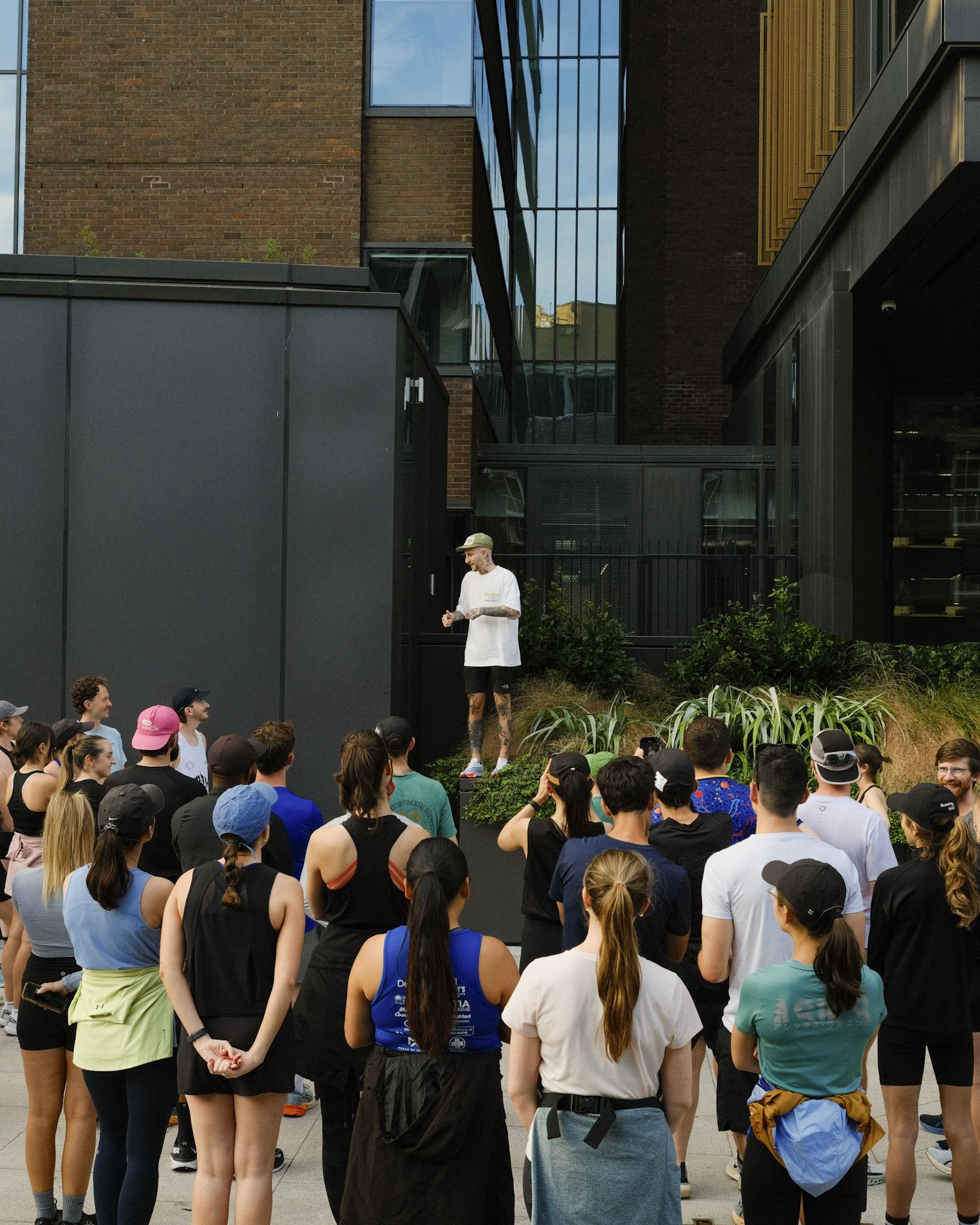 A man standing on a raised platform addressing a crowd outside a modern building with glass and brick architecture.