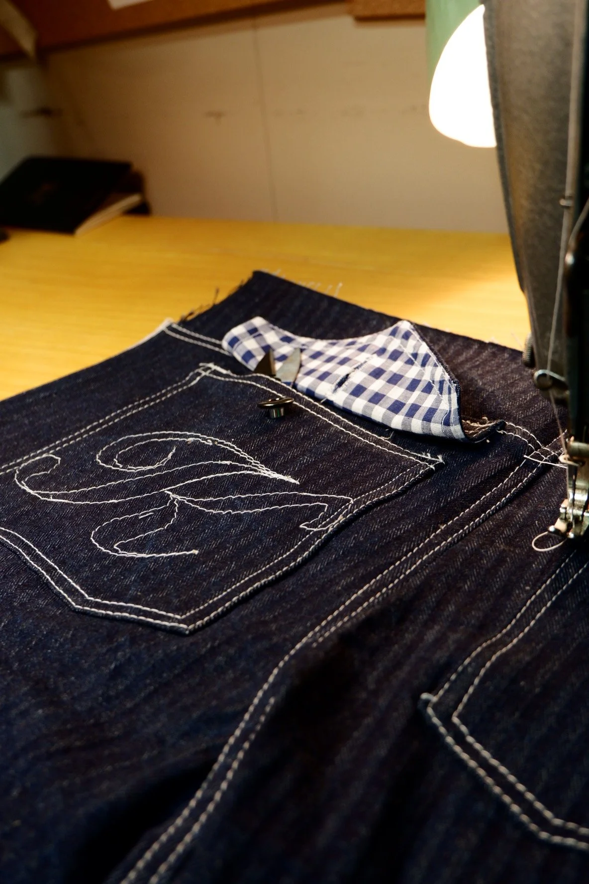 Close-up of dark denim jeans with white stitching and a pocket with a blue and white checkered fabric lining.