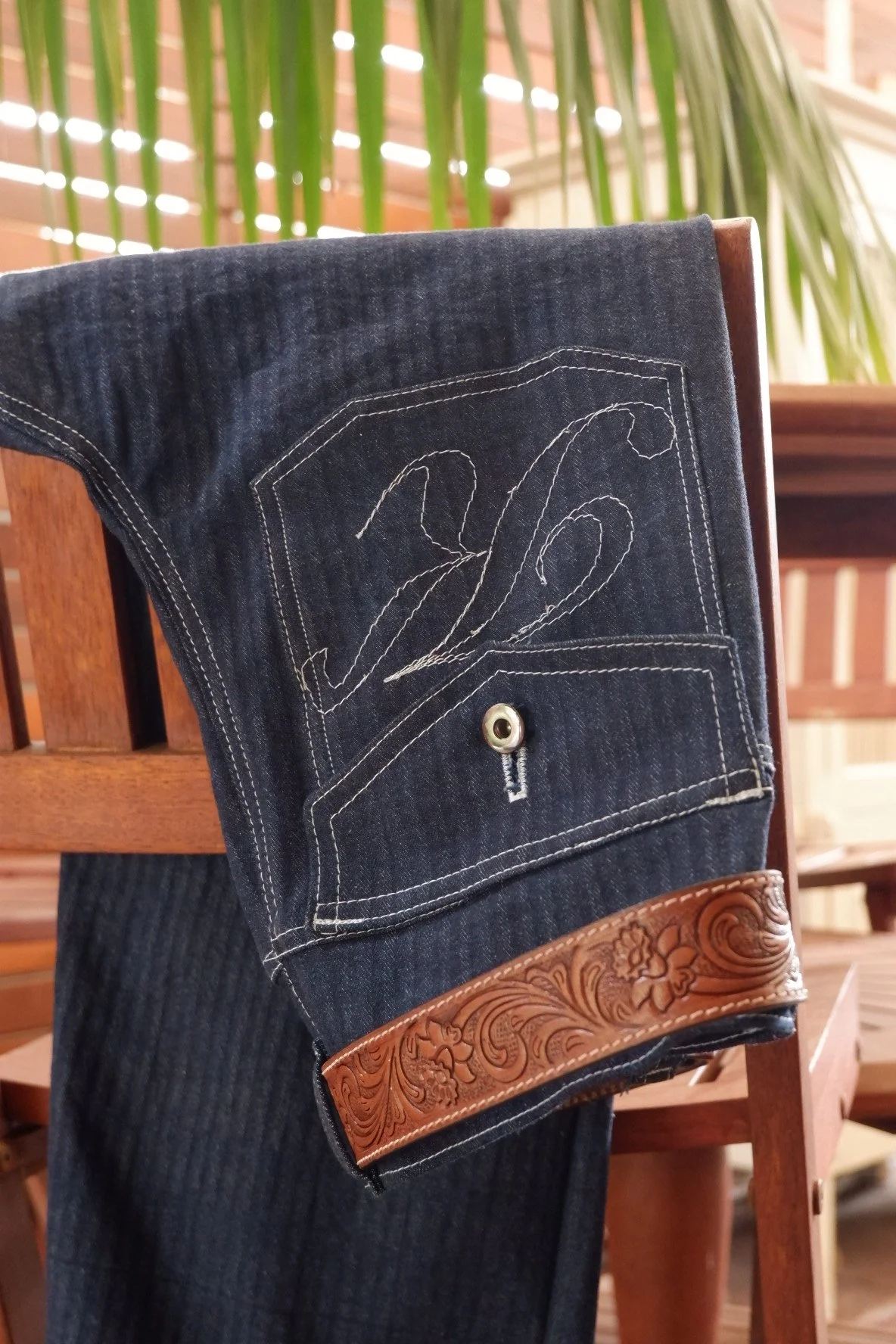 Pair of dark blue denim jeans with a front pocket, displaying white stitching and a decorative brown leather patch at the bottom of the pocket.