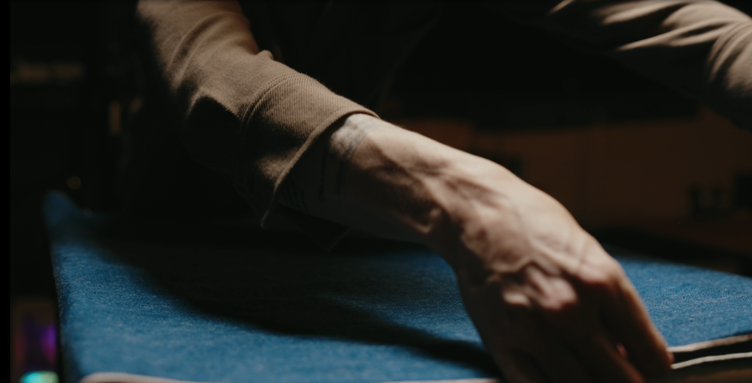 Close-up of a person's arm with tattoos resting on a blue surface, under warm lighting.