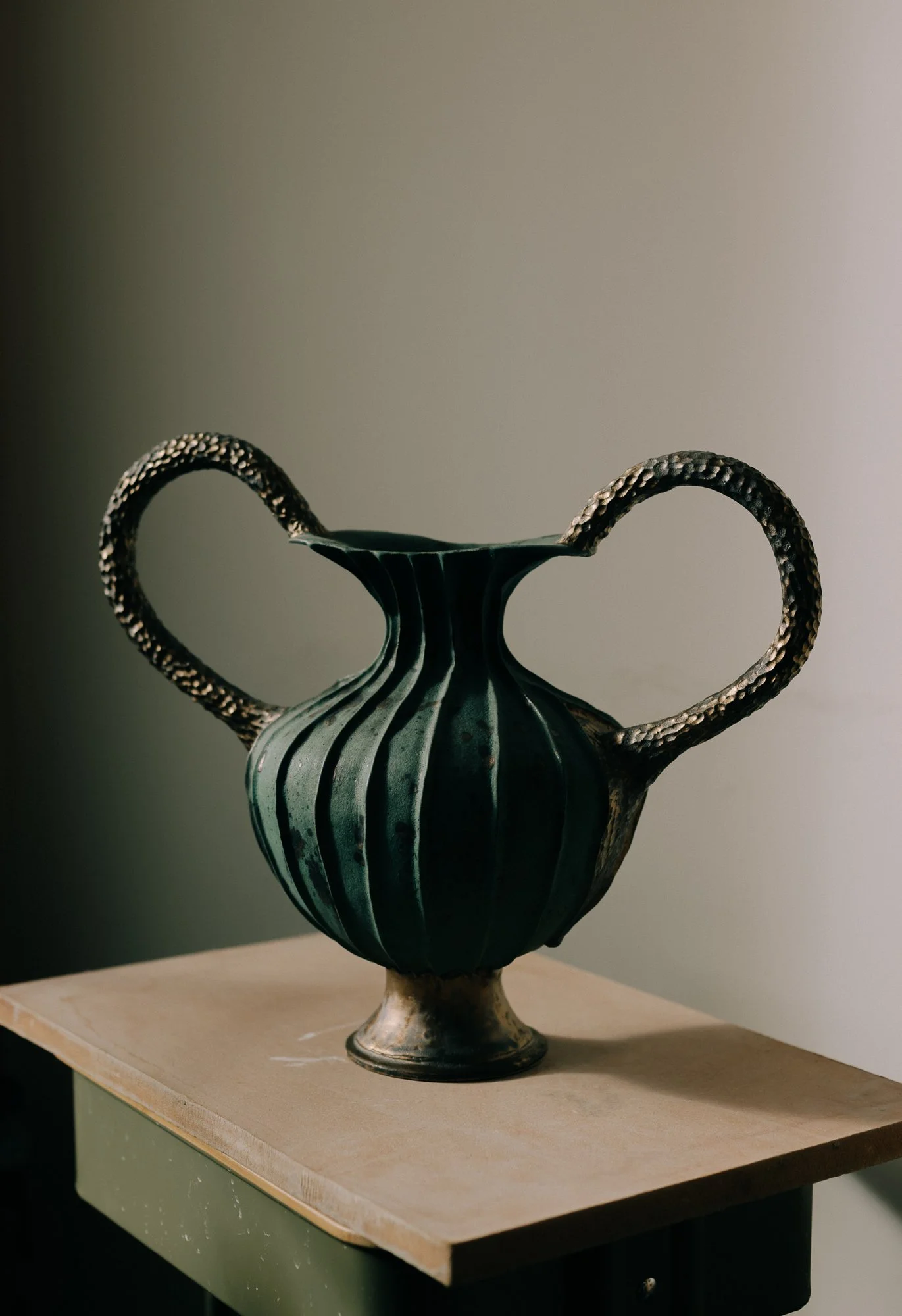 A decorative vase with a unique handle design, sitting on a small wooden table against a plain background.