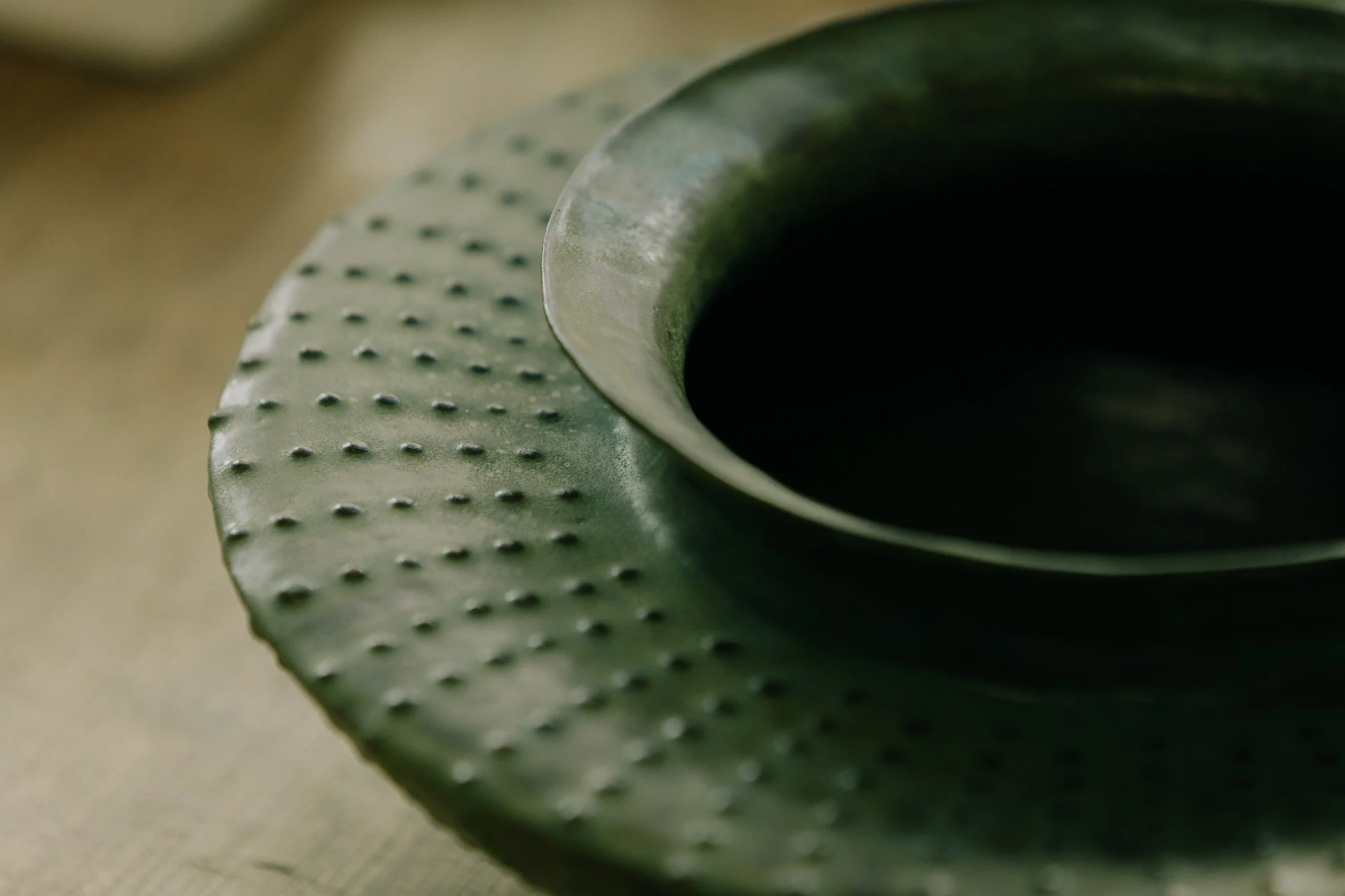Close-up of a green ceramic bowl with a textured, dotted rim, filled with a dark liquid.